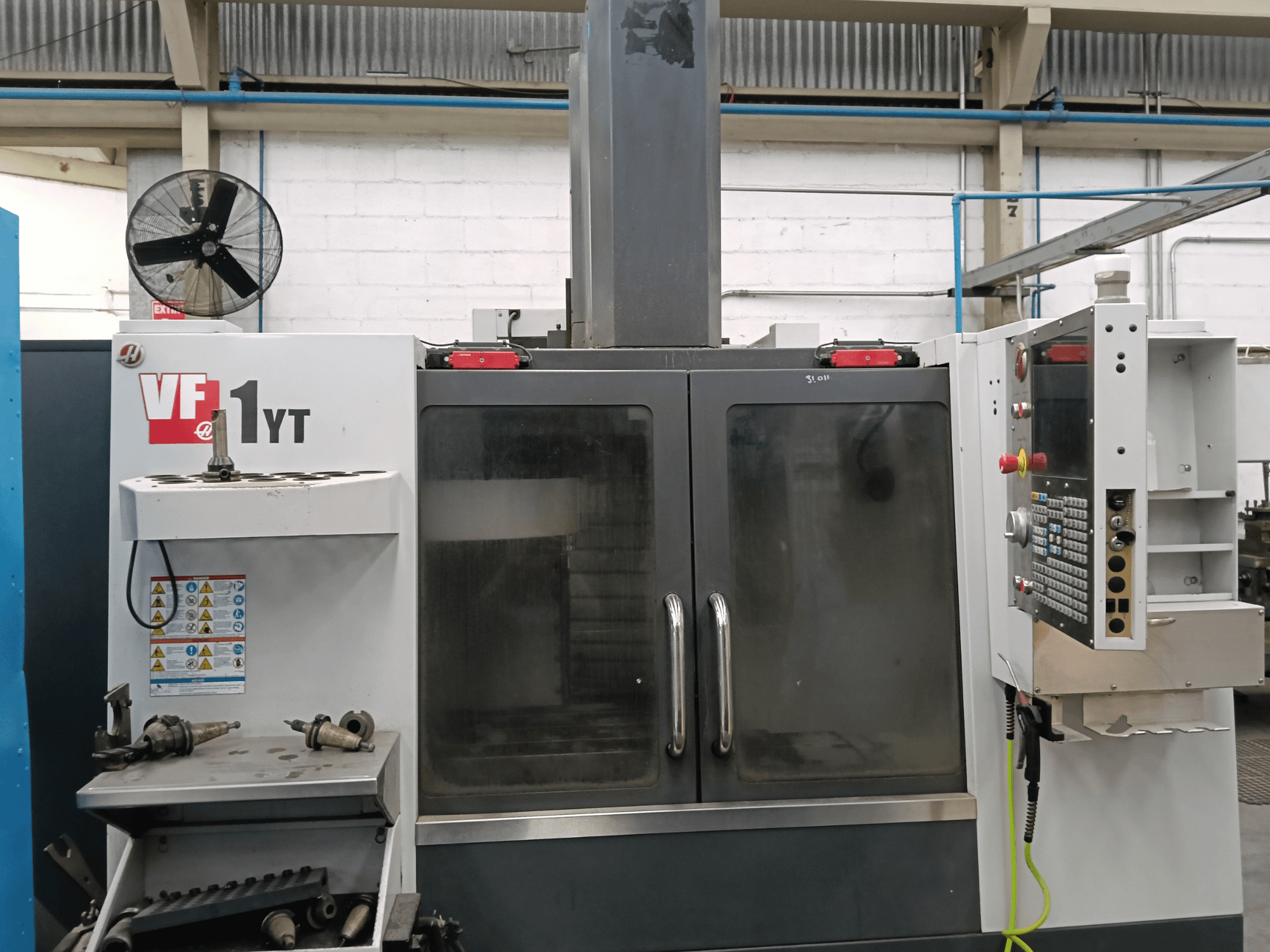 HAAS VF-1YT-1 vertikaalse töötlemiskeskuse vaade eest, kus küljel on juhtpaneel ja tööriistad.