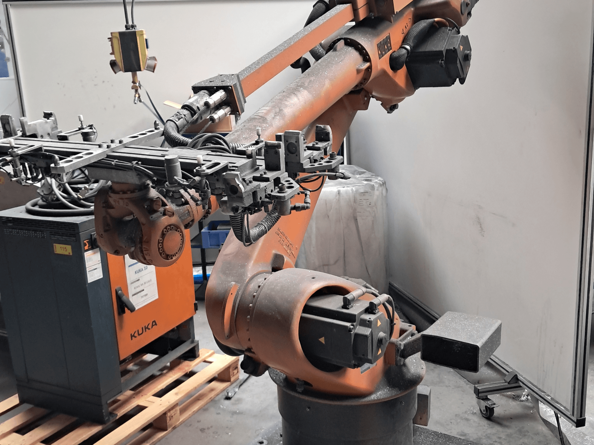 KUKA KR 30L16-2 robotkäsi külgvaates, millel on keerukas tööotsik ja juhtkaablid, asub KUKA juhtpaneeli kõrval.