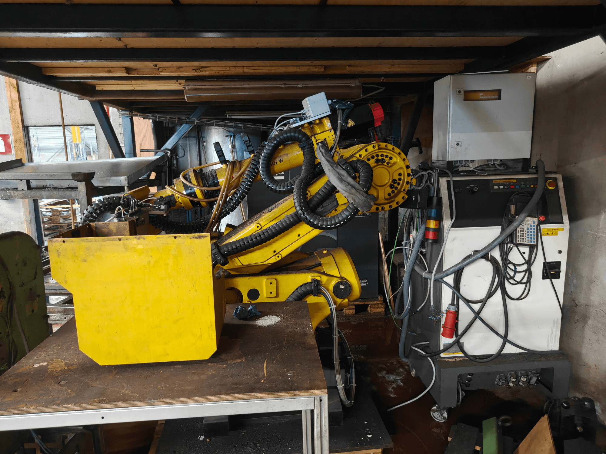 FANUC S-430i W robotkäe esivaade: kollane, koos juhtpaneeli, kaablite ja tööpingil asuva kollase komponendiga.