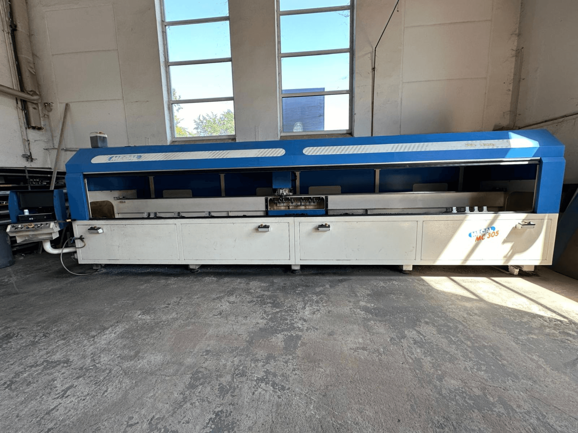 MECAL MC 305 vertikaaltöötluskeskuse esiplaan, millel on sinine ja valge disain, nähtav töölaud ja juhtpaneel.