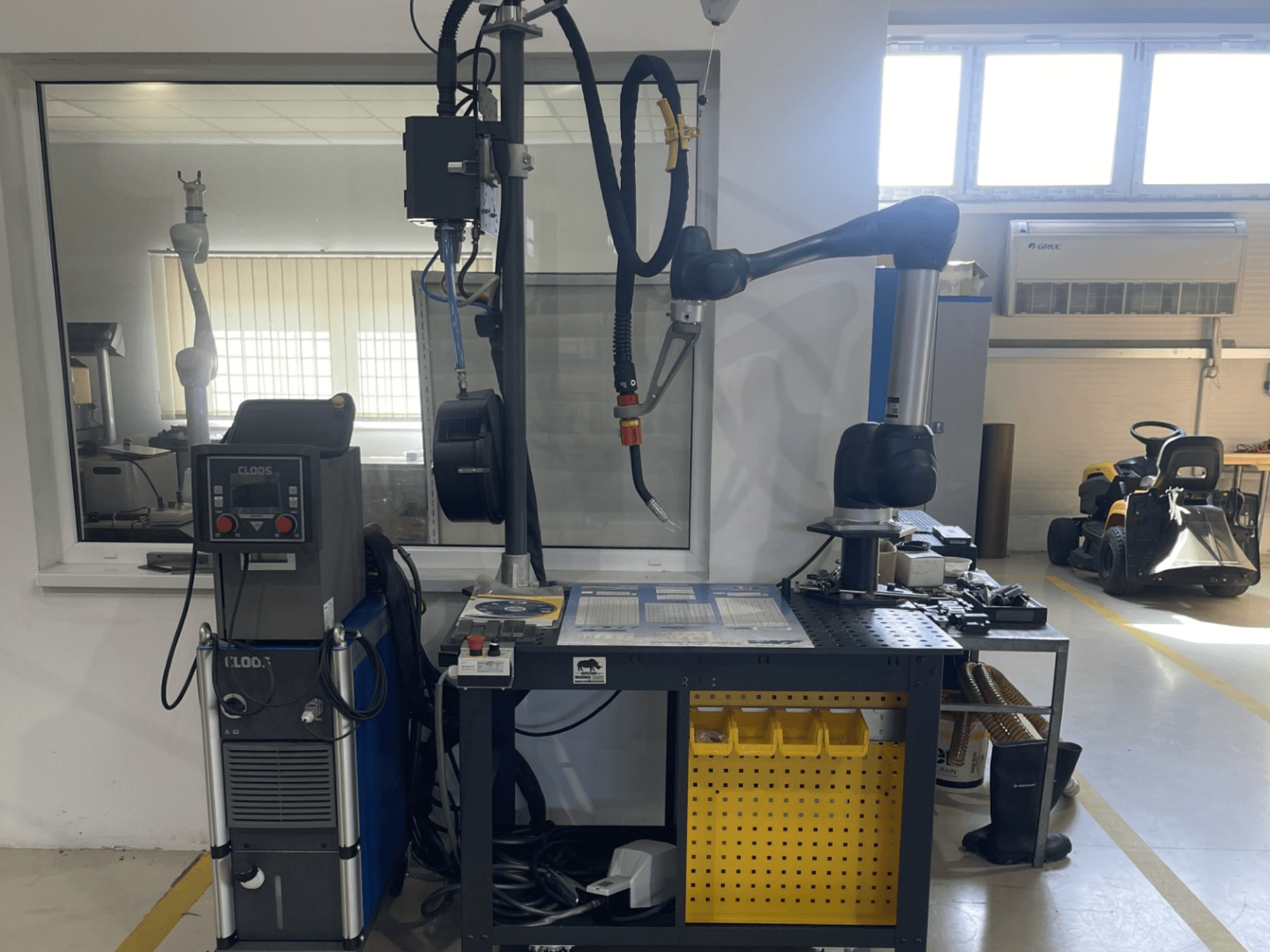 DOOSAN M1013 koostöörobot töökodas, külgvaade, kus tööpingil on keevitusseadmed ja tööriistad.