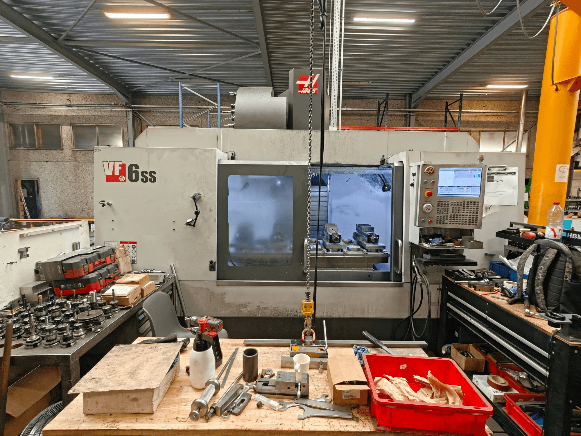 Haas VF-6SS vertikaalne töötlemiskeskus töökodas, külgvaade, millel on näha juhtpaneel ja tööala, mis on täis tööriistu.