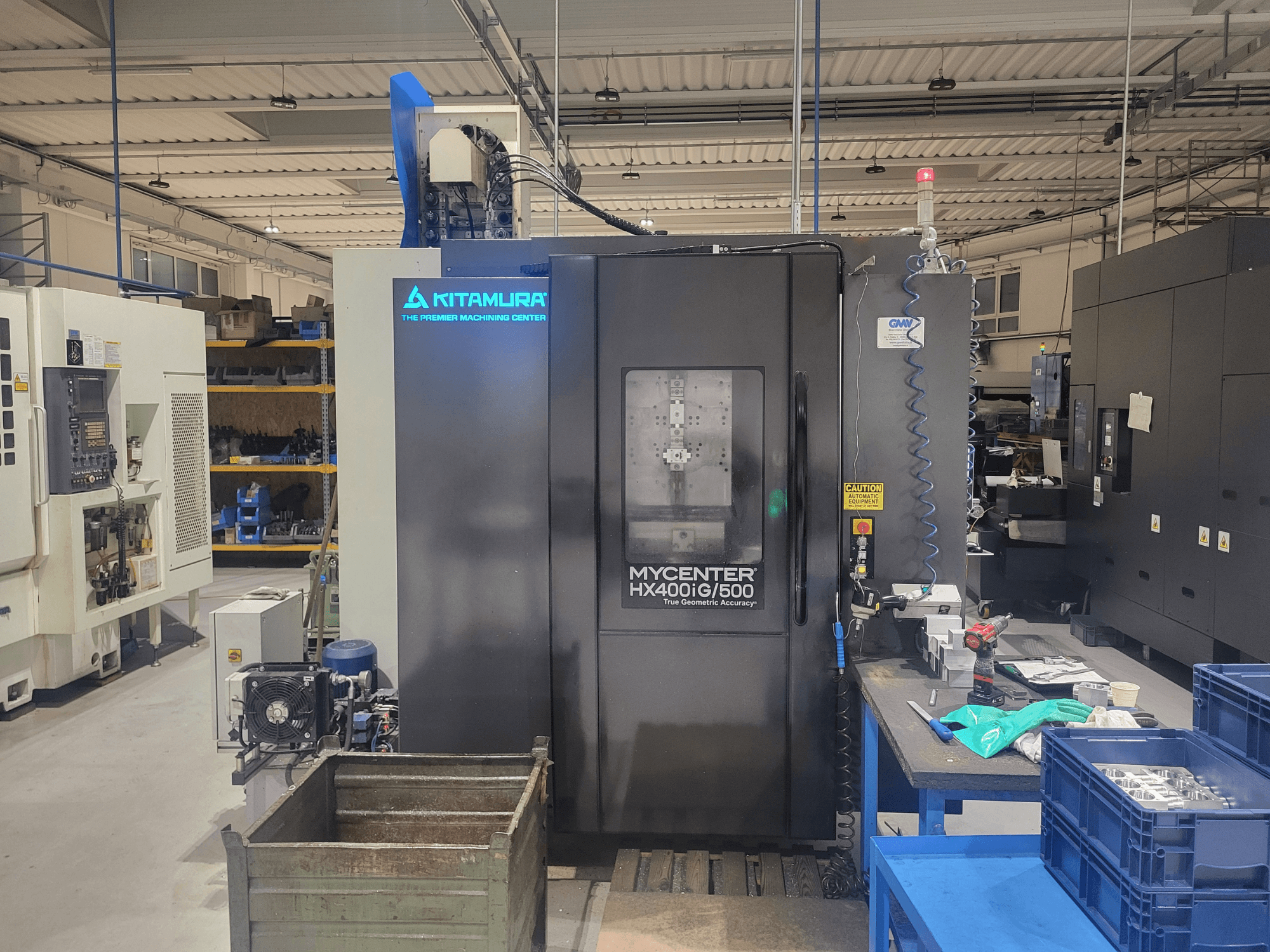Kitamura Mycenter HX400iG/500 CNC-tööpink töökojas, esivaade, juhtimispuldid, tööriistade hoidla ja materjalid lähedal.
