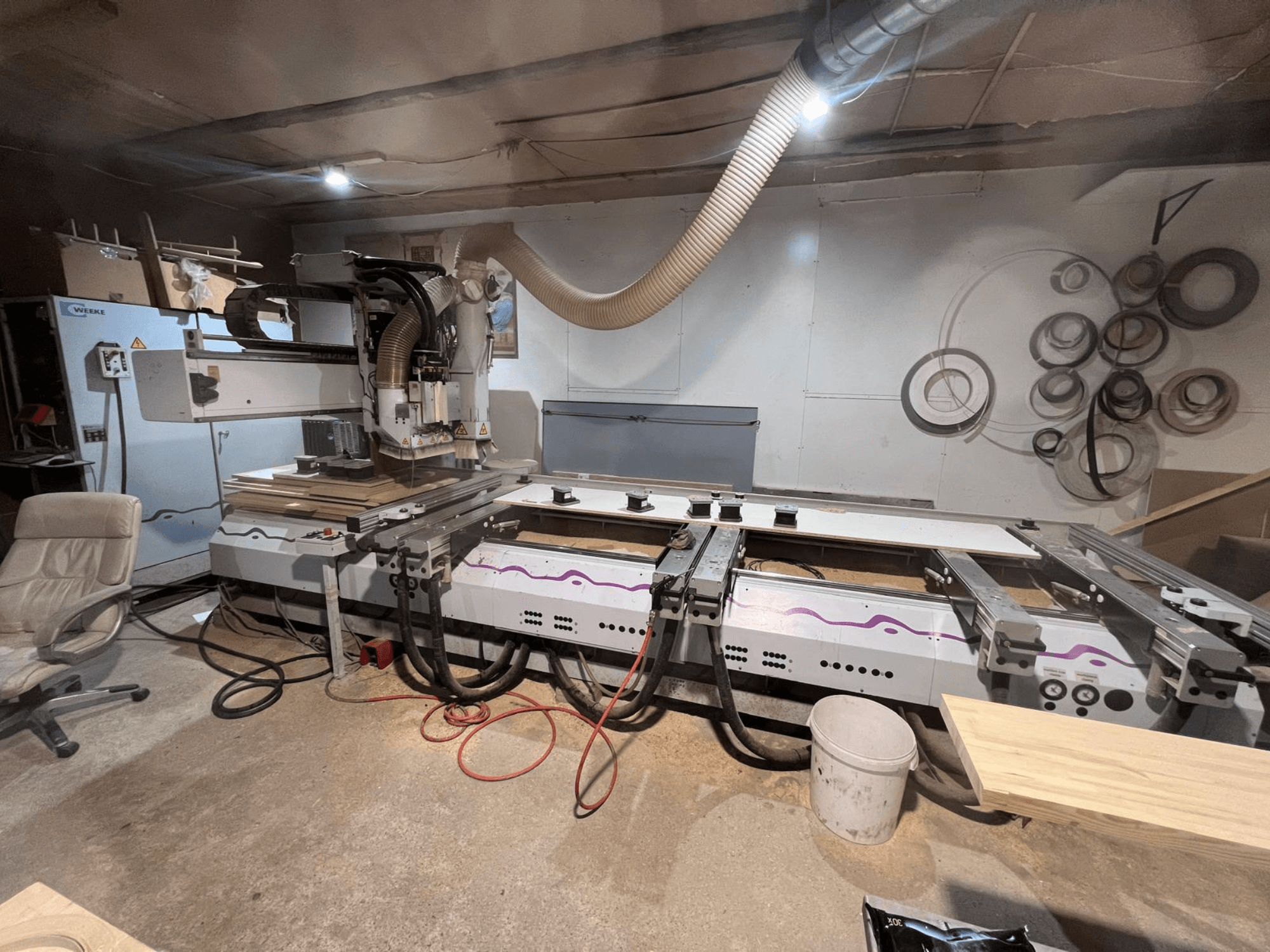 Töökojas asuv CNC-puidutöötluskeskus Weeke OPTIMAT BP 120, vaade eest, kus on näha puit tükid ja tööriistad tööpinnal.