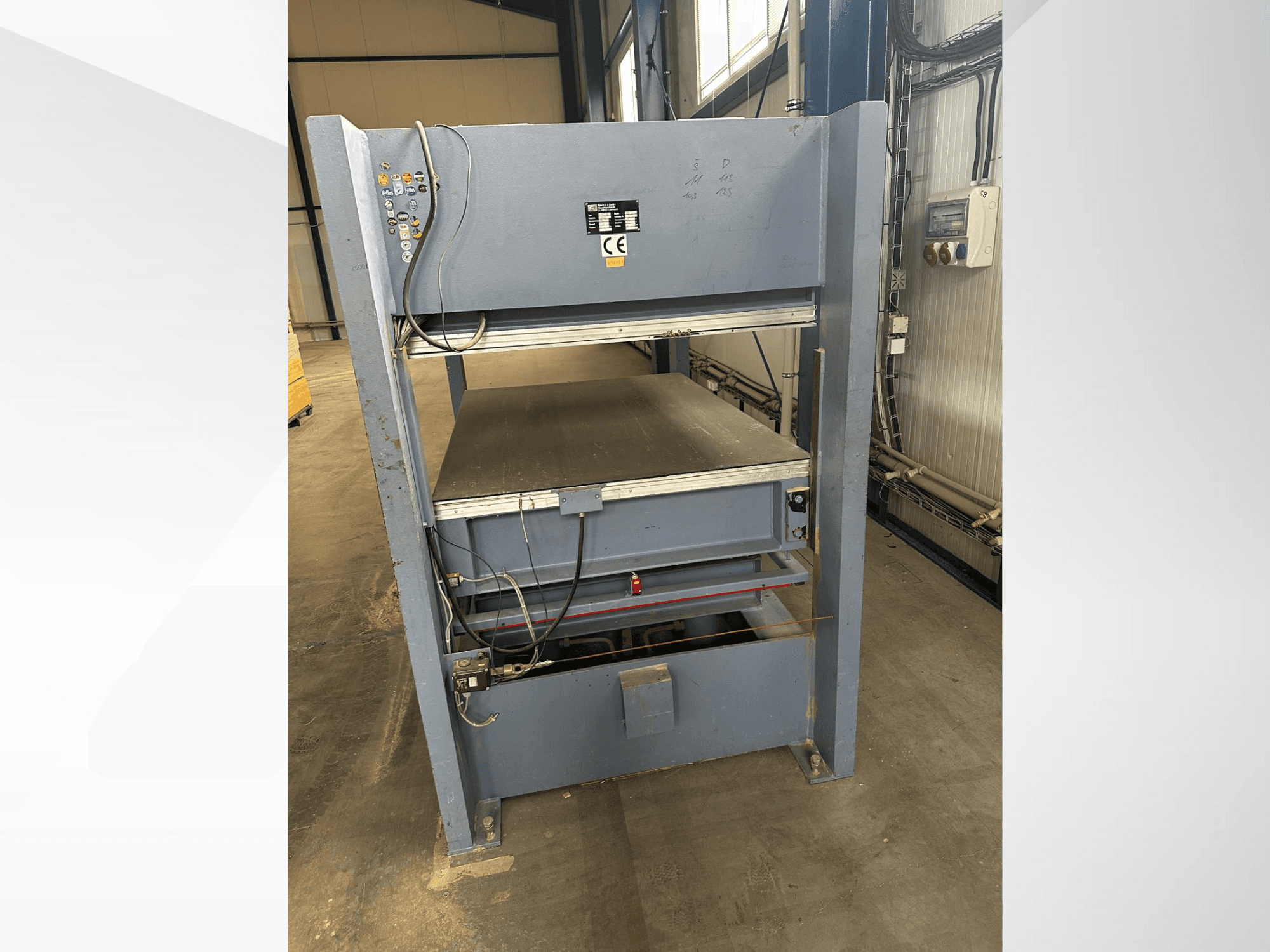 Hall tööstuslik masin juhtpaneeliga, vaadatuna eestpoolt; sisaldab reguleeritavaid platvorme ja ohutusmärke.
