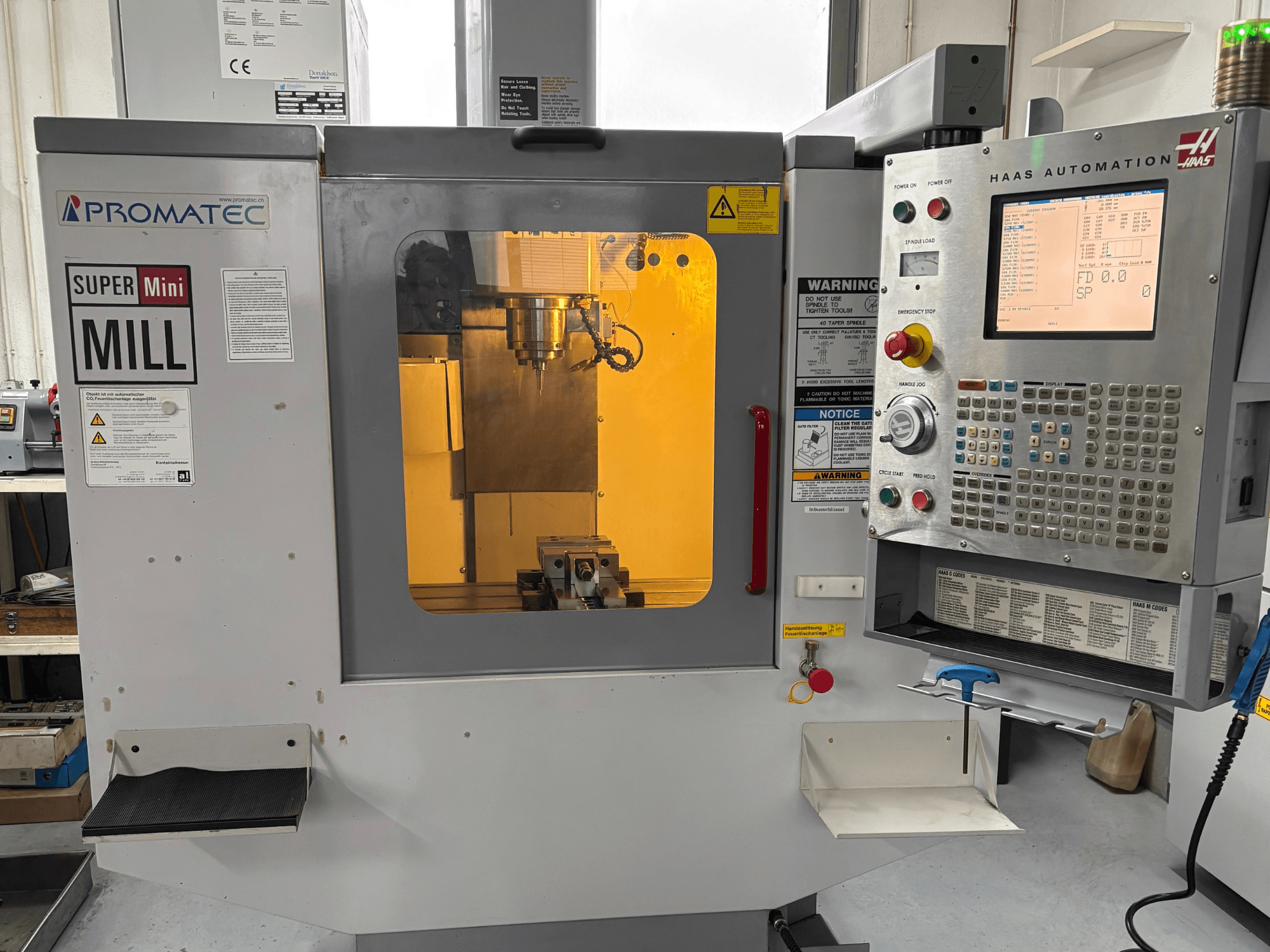 Promatec Super Mini Mill esiplaanil, varustatud Haas Automationi juhtpaneeliga ja nähtava lõiketööriistaga sees.