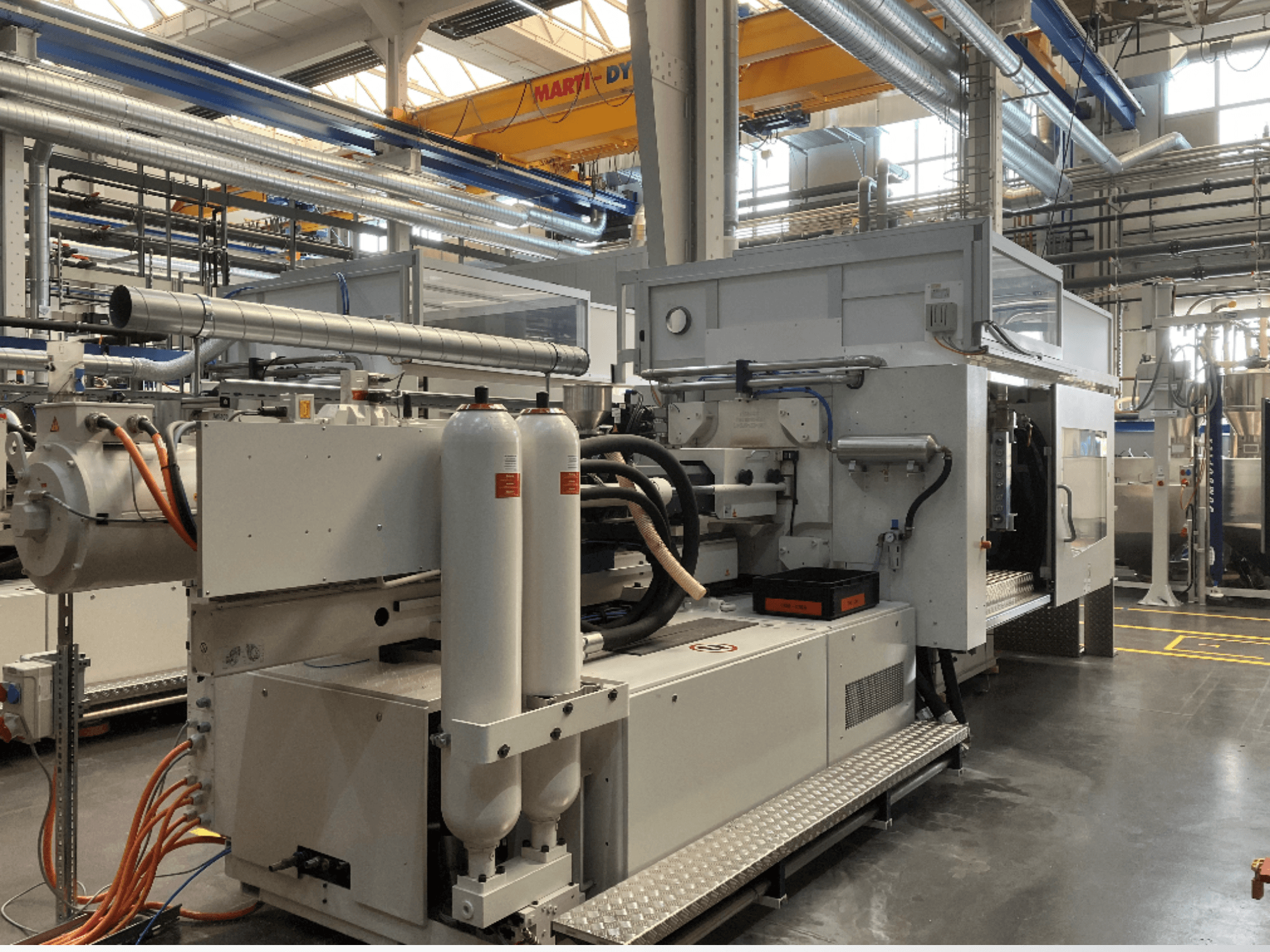 Tööstusmasin külgvaates koos mitme vooliku, kahe vertikaalse mahuti ja juhtpaneeliga; mark/mudel ei ole nähtav.