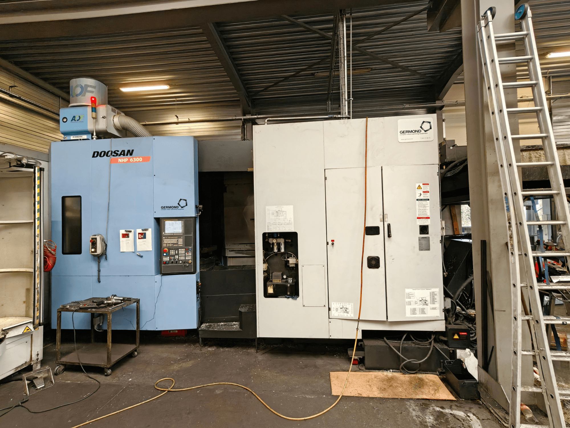 DOOSAN NHP6300 horisontaalne töötlemiskeskus eestvaates, millel on näha juhtpaneel ja selle kõrval asuvad masinad töökoda keskkonnas.
