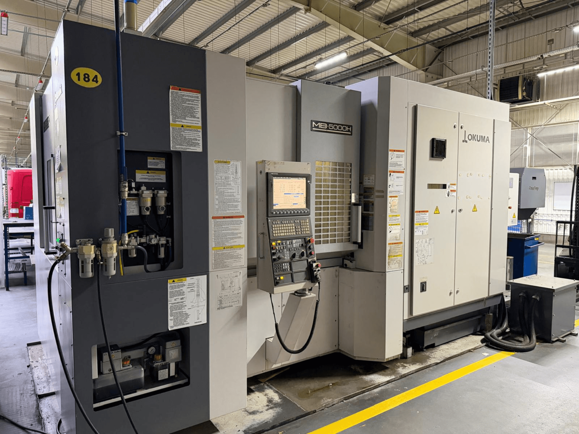 Okuma MB 5000H horisontaalne töötluskeskuse esivaade, millel on juhtimisseadmed, märgistus ja hüdraulilised ühendused.