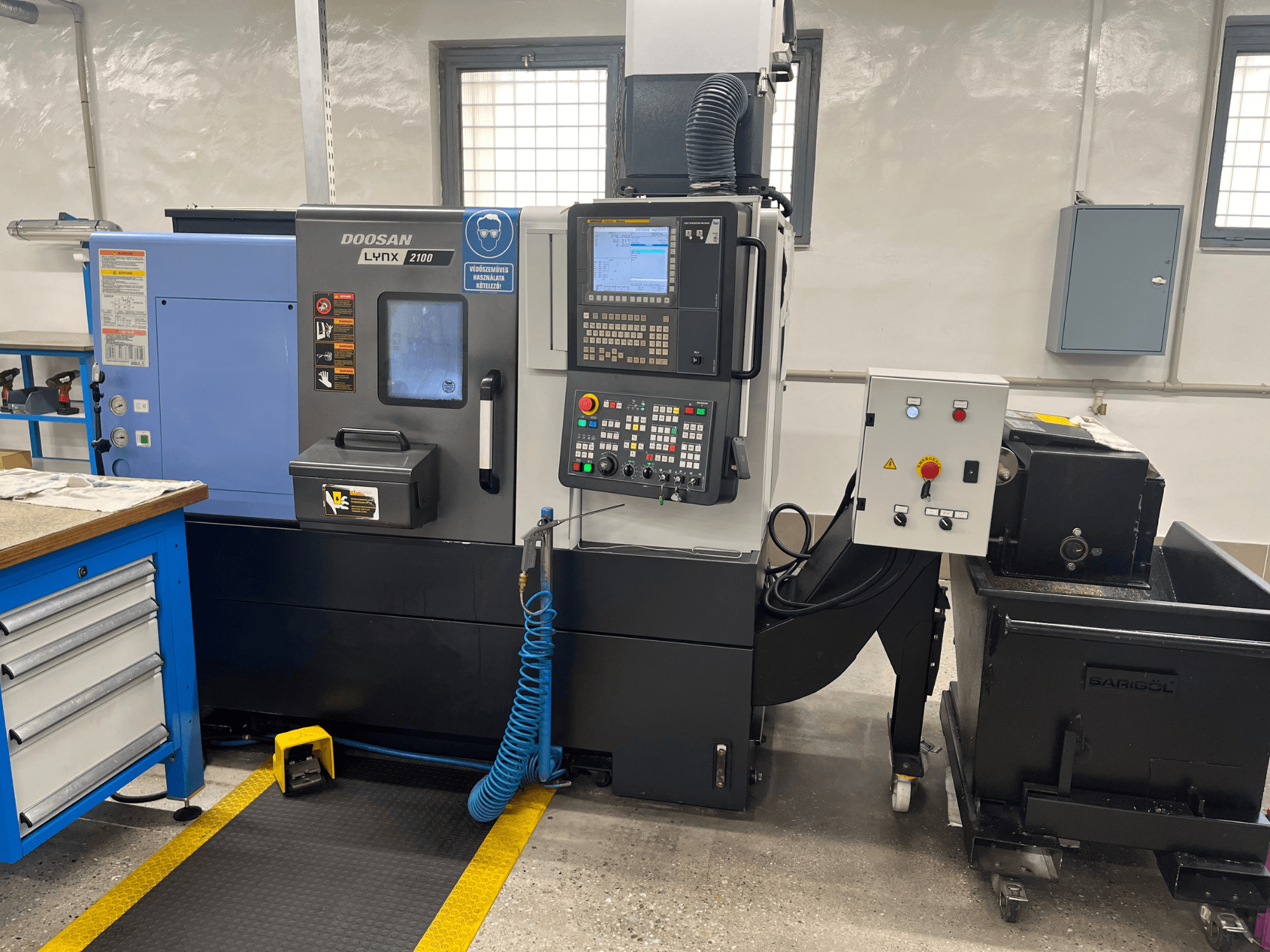 Doosan Lynx 210 treipink töökojas, kus on näidatud juhtpaneel, tööriistade hoidmine ja jahutusvedeliku süsteem, külgvaade koos tööruumi detailidega.