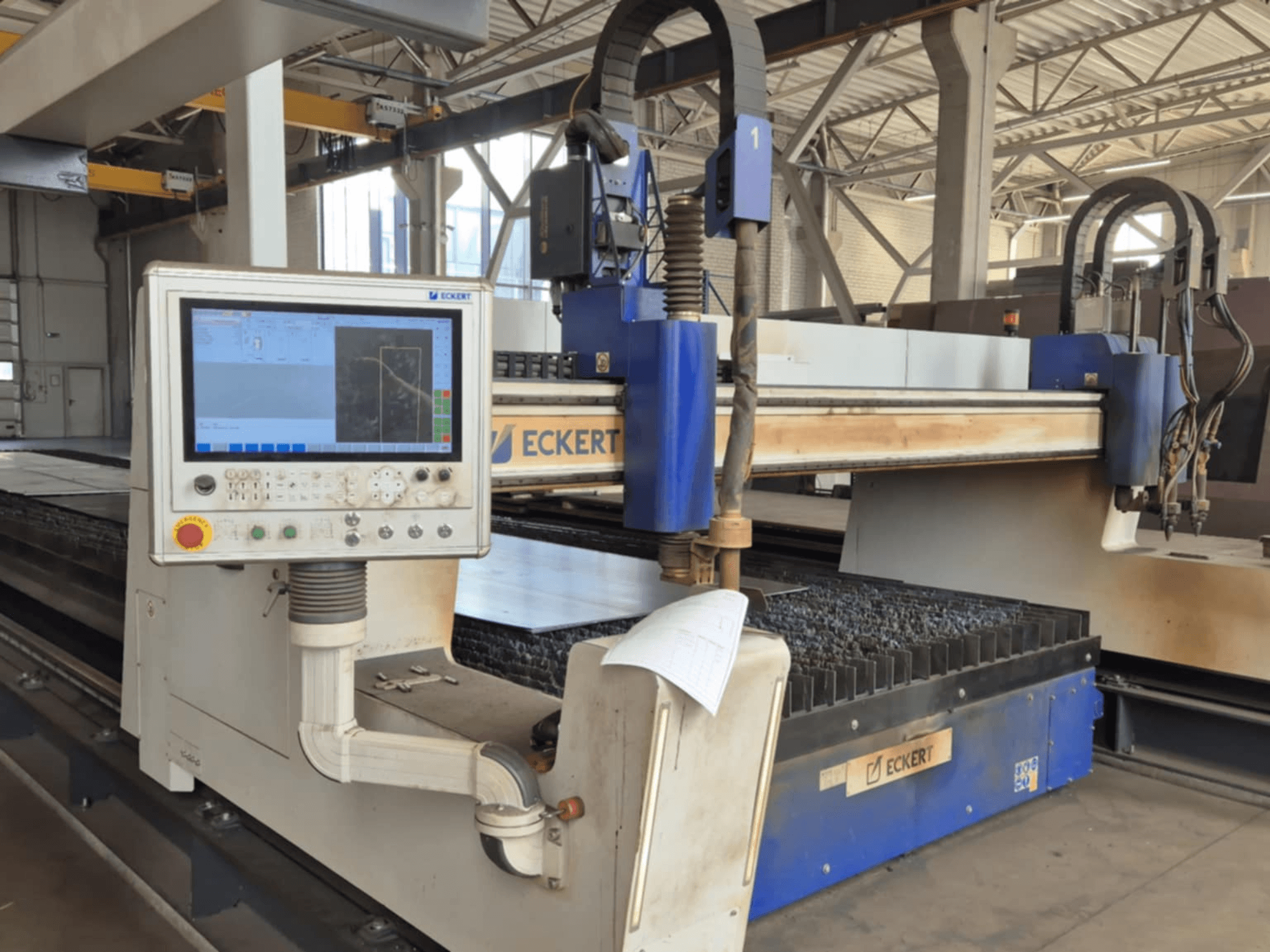 ECKERTi CNC-lõikepingi juhtpaneel esiplaanil, millel on puutetundlik ekraan ja mitmesugused juhtimisnupud.