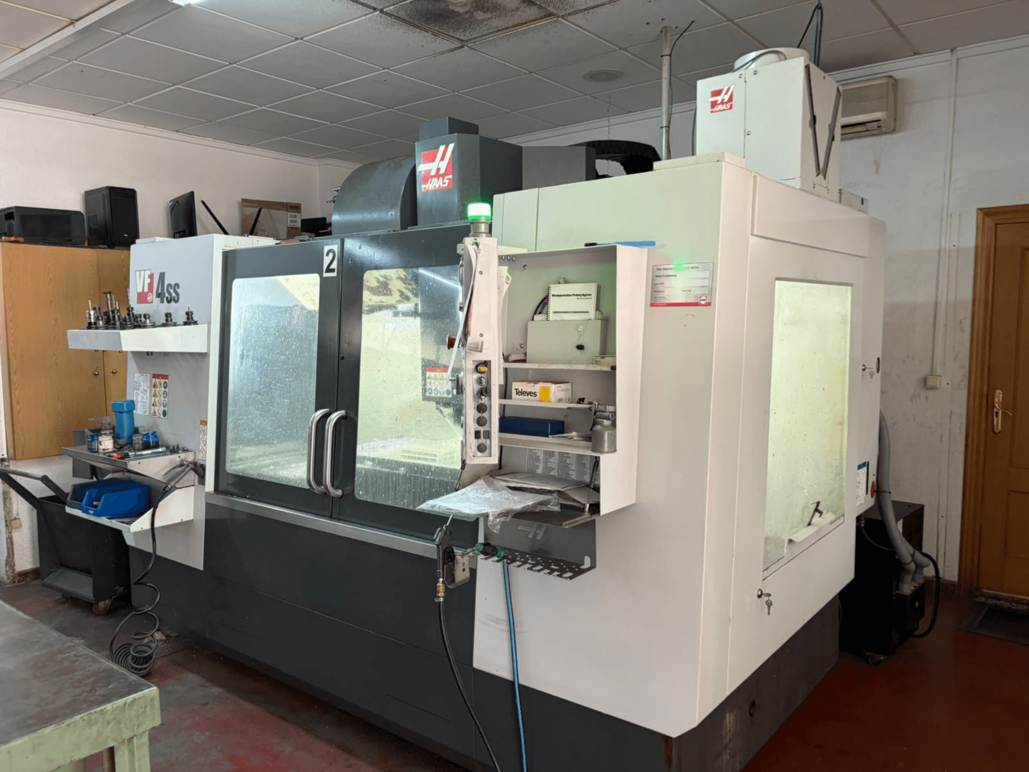 HAAS VF 4SS vertikaalne töötlemiskeskus töökodas, vaade eest, millel on näha juhtpaneel ning töötsoon koos tööriistade ja materjalidega.