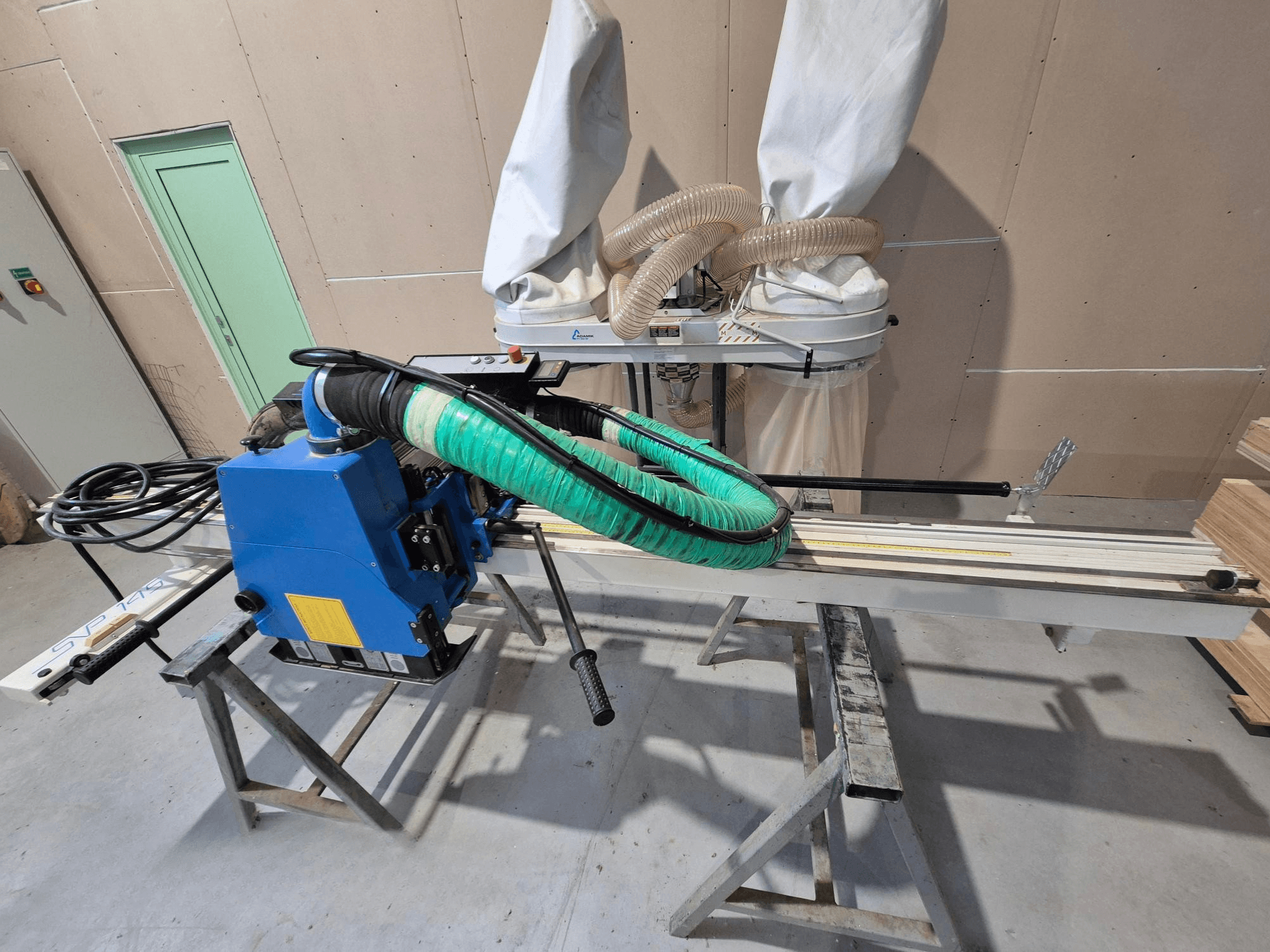 Sinine SVP-175 horisontaalne plaadisaag koos rohelise tolmuvooliku ja toega, küljelt vaadatuna töökojas.