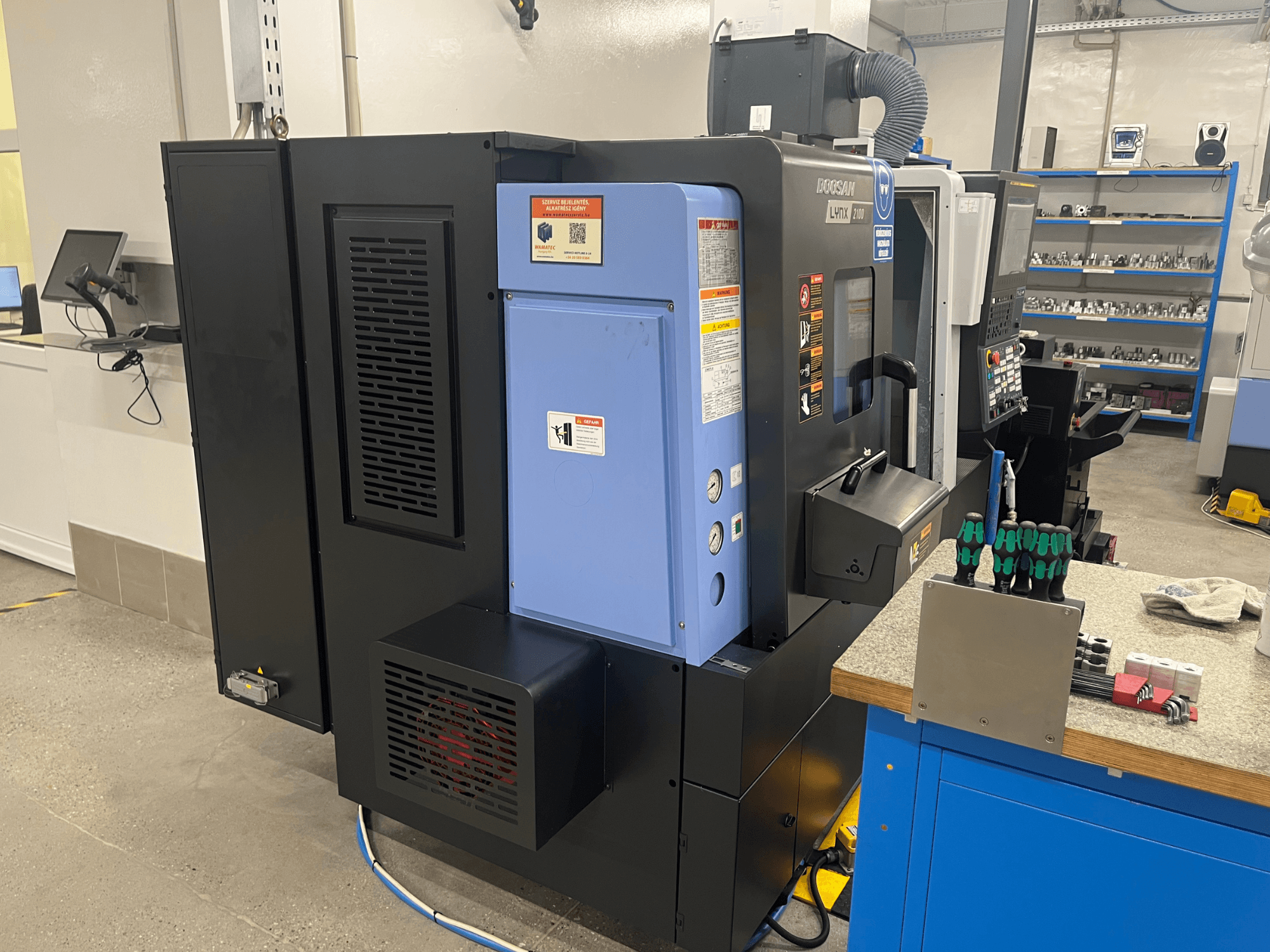 Doosan Lynx 2100 treipingi külgvaade, kus on näidatud juhtpaneel, ventilatsioonisüsteem ja tööriistad töölaual.