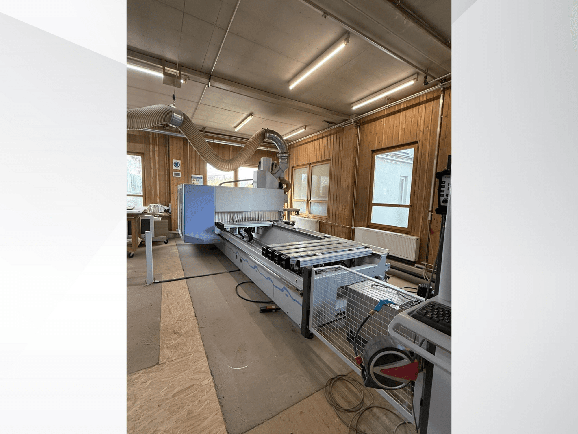 CNC-freesimispink töökojas, külgvaates, millel on suur sinine korpus, lisatud lintkonveier ja nähtav juhtpaneel.