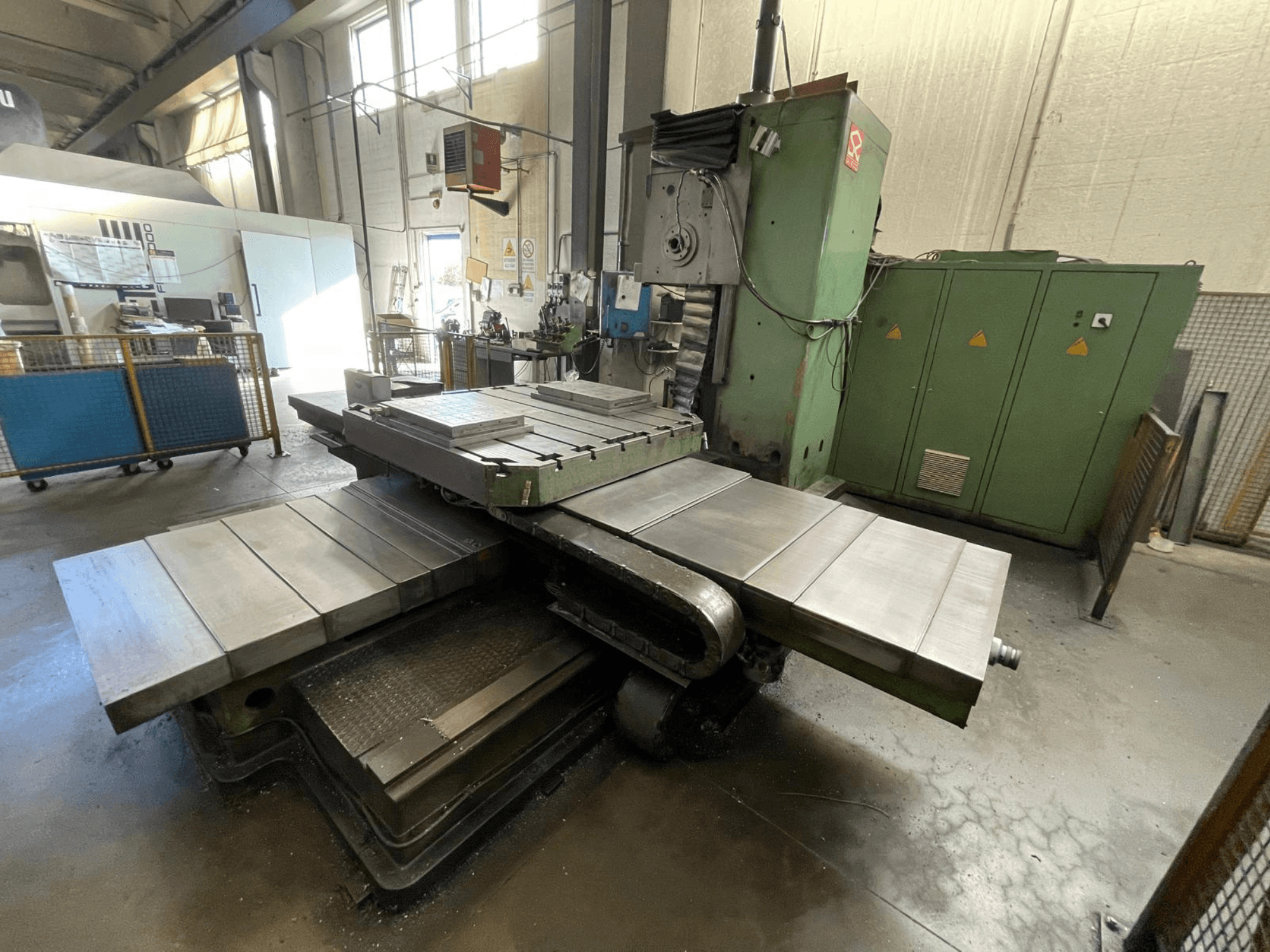 Suur tööstuslik freespink rohelise korpusega, külgvaates, millel on mitu tasast pinda ja tagaplaanil hoiukapid.