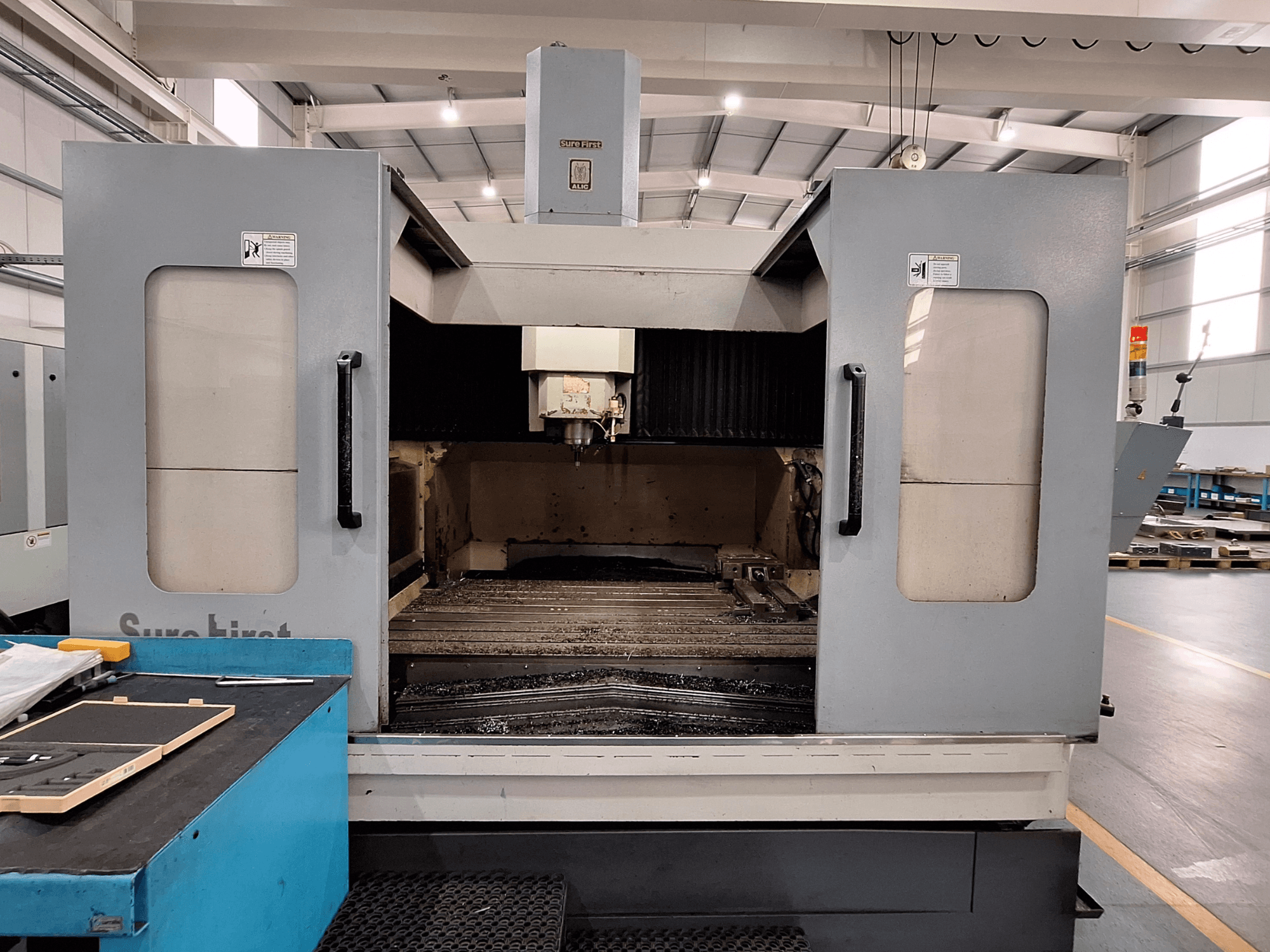 Vertikaalne töötluskeskus Sure First QM-1836, esiplaanil tööriistapea ja tühi tööala, kaasaegne tööstuslik seade.