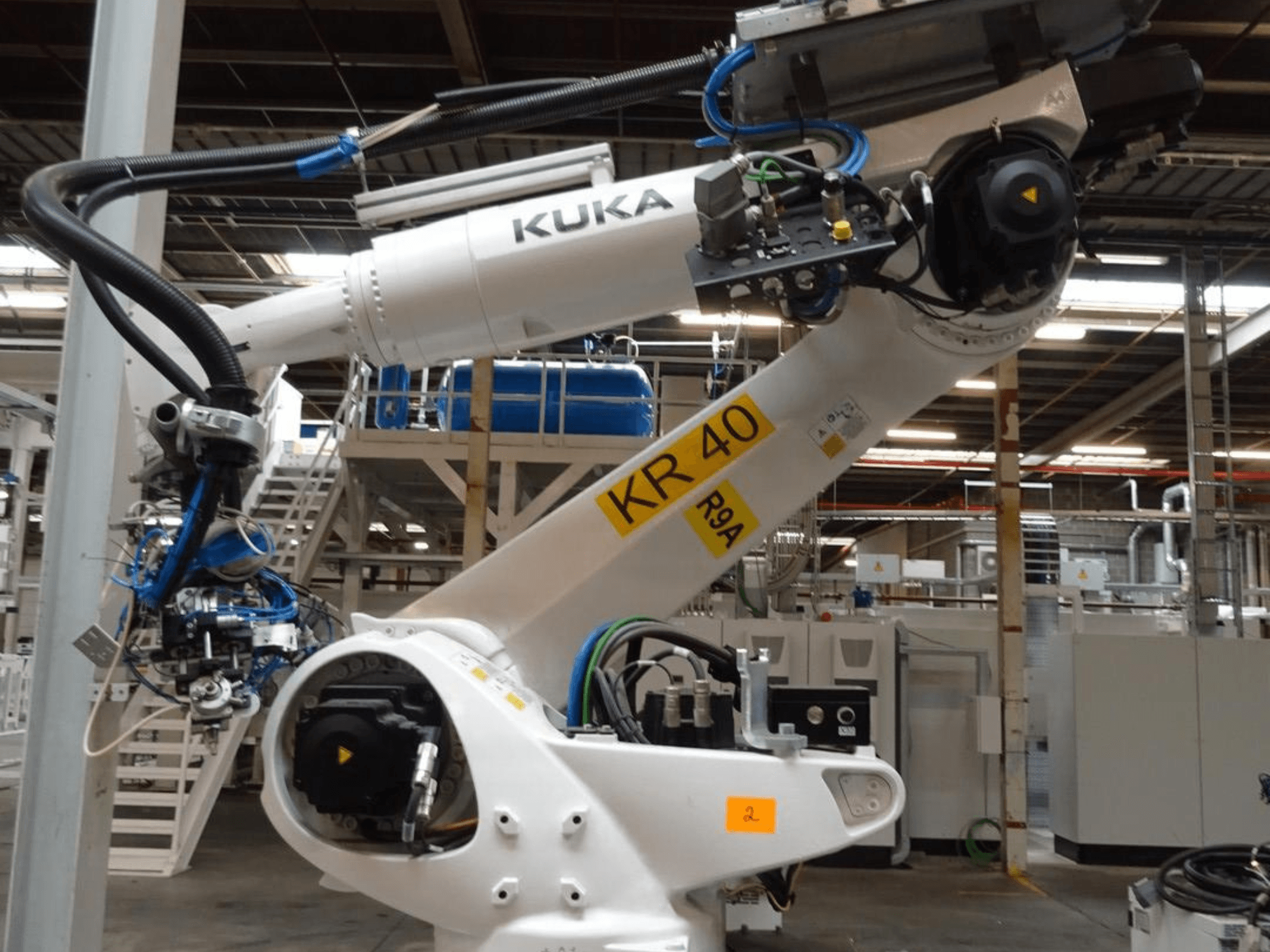 KUKA KR 120 R3100-2 robotkäsi külgvaates, kus on näidatud juhtpaneel ja mehaanilised komponendid tööstuskeskkonnas.