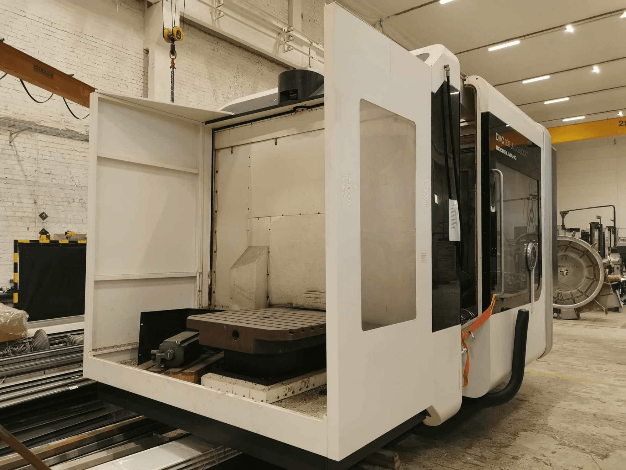 DMC 100U lineaarne CNC-tööpink, külgvaade avatud ligipääsuuksega, millel on näha töölaud ja sisemised komponendid.