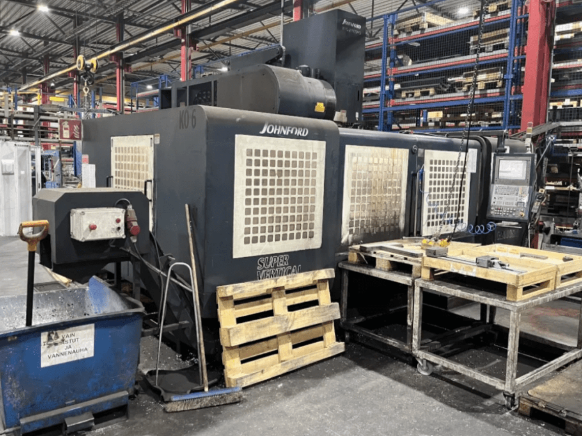 Johnford Super vertikaalne freespink tehases, külgvaade juhtpaneeli, kaubaaluste ja puhastusseadmete lähedal.