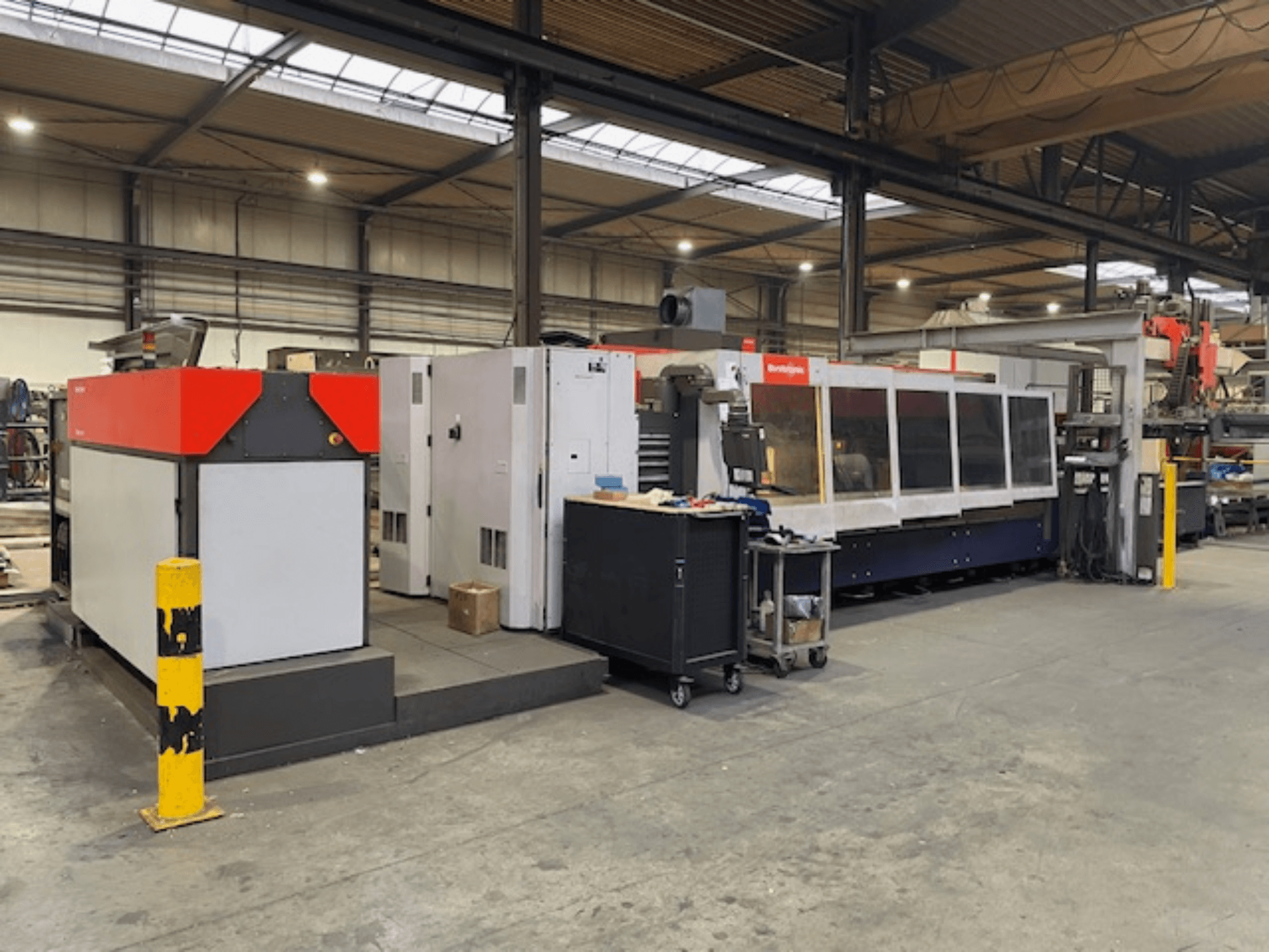 Bystronic BySpeed 3015 CO2-laserlõikepink, külgvaade töökojas, millel on erinevad punased ja hallid disainielemendid.