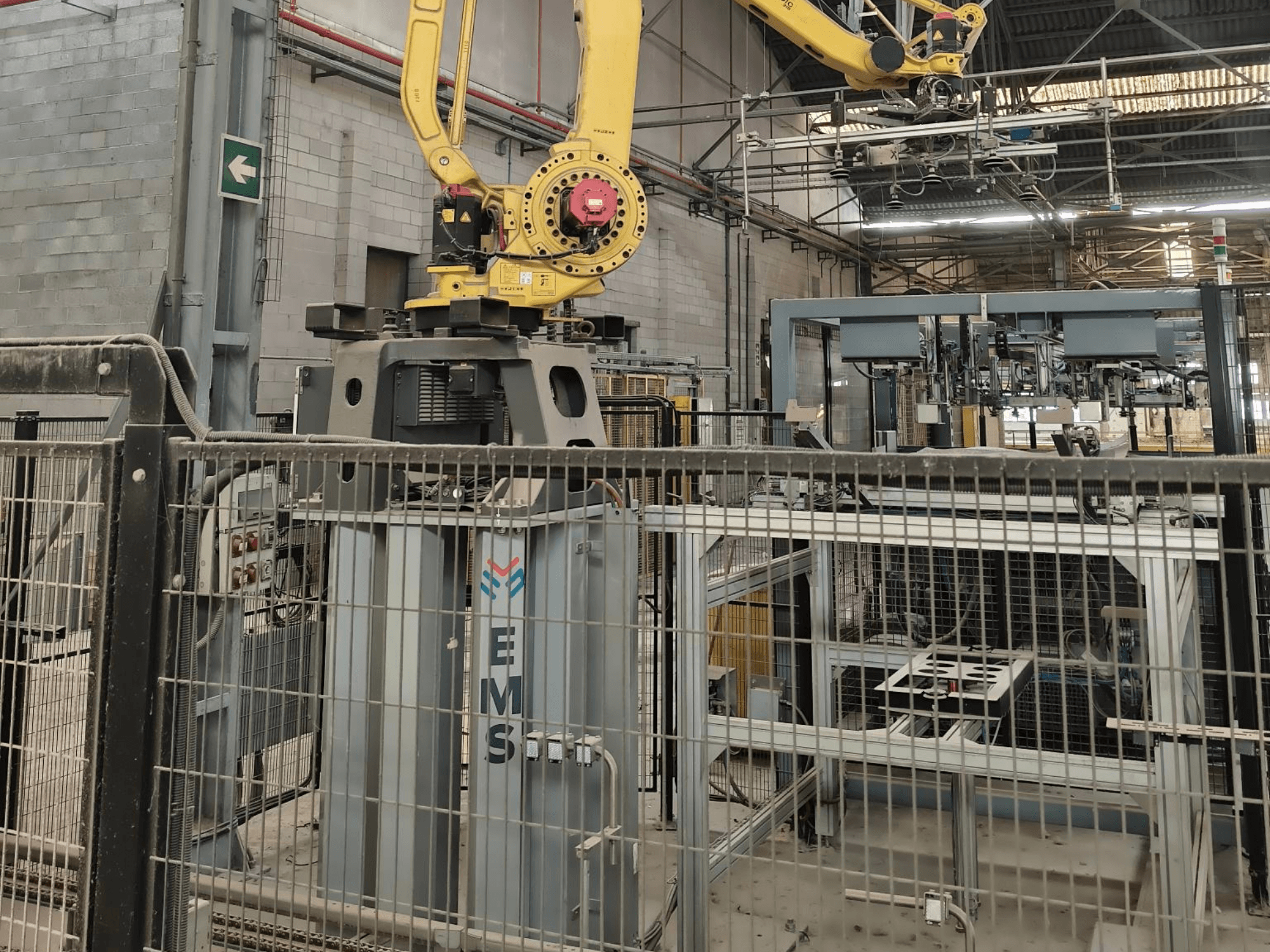 FANUC M-410iC/315 robotkäe esivaade, mis on paigutatud EMS-tööriista kohale, taustal on tööstusseadmed ja piire.