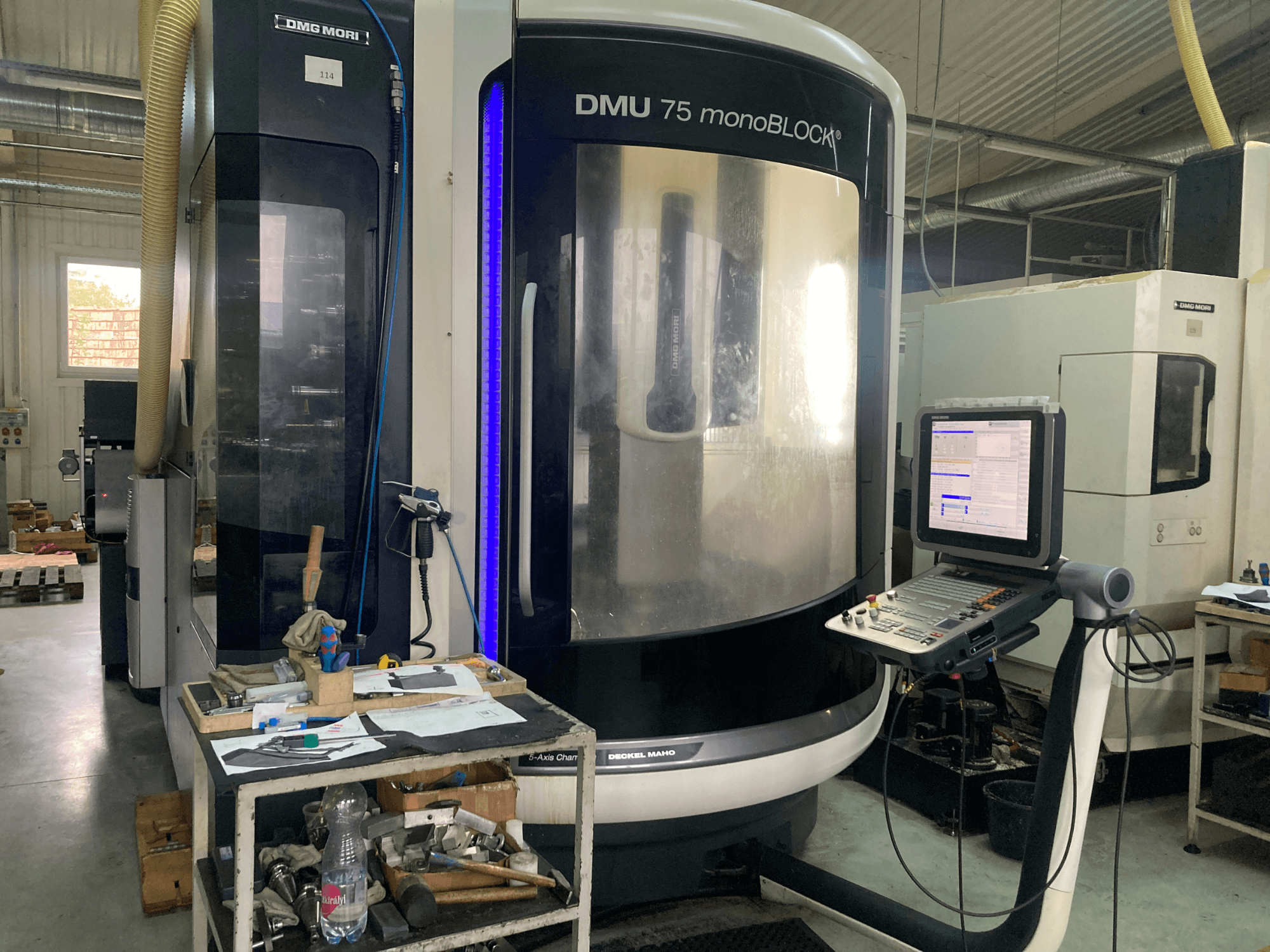 DMG MORI DMU 75 monoBLOCK® CNC-pink, esiplaan, kus on juhtpaneel, tööriistad ja tööruum koos materjalidega.