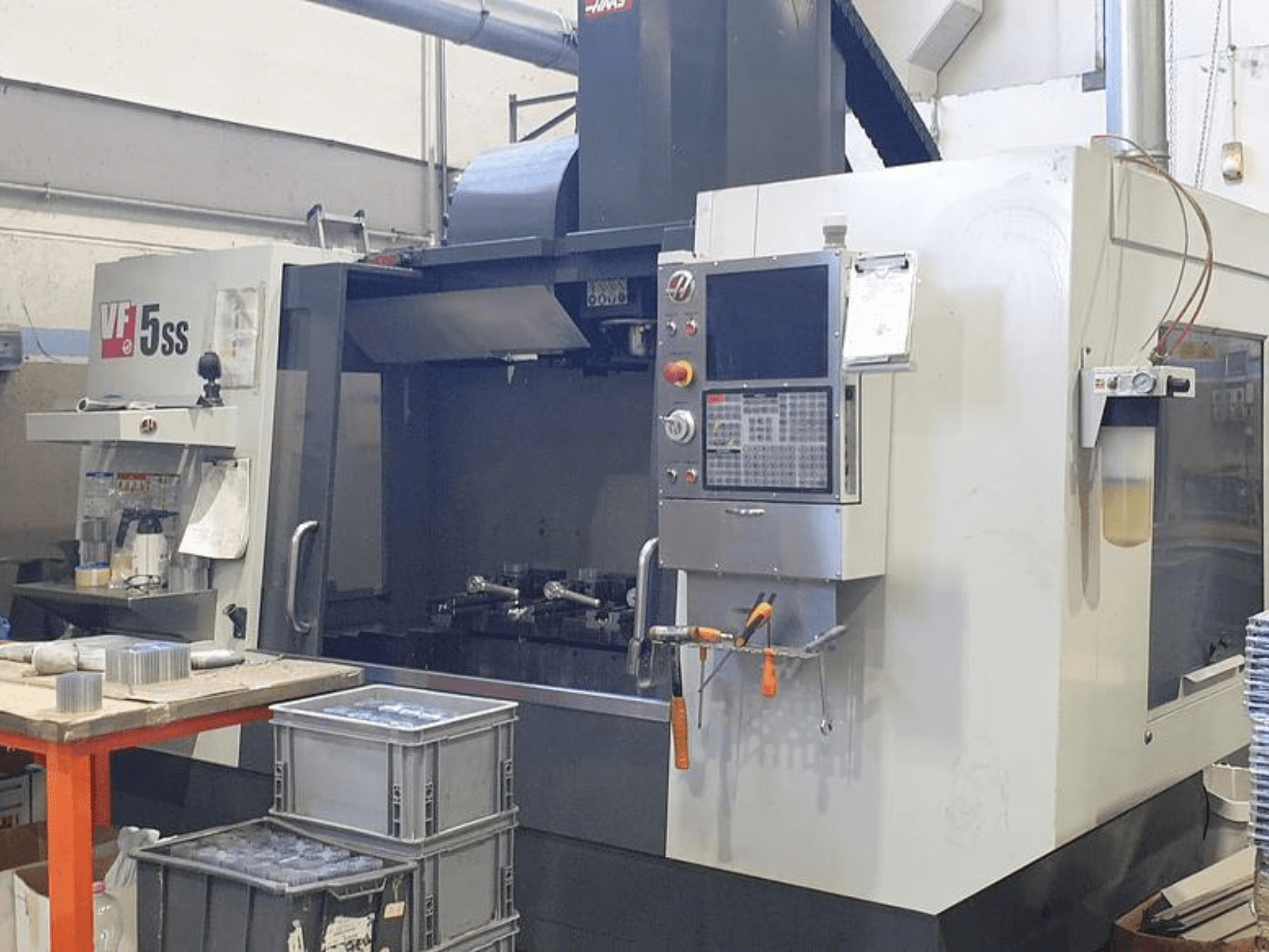 HAAS VF-5SS vertikaalne töötlemiskeskus esiplaanil, kus on näidatud juhtpaneel, tööruum ja hoiukastid.