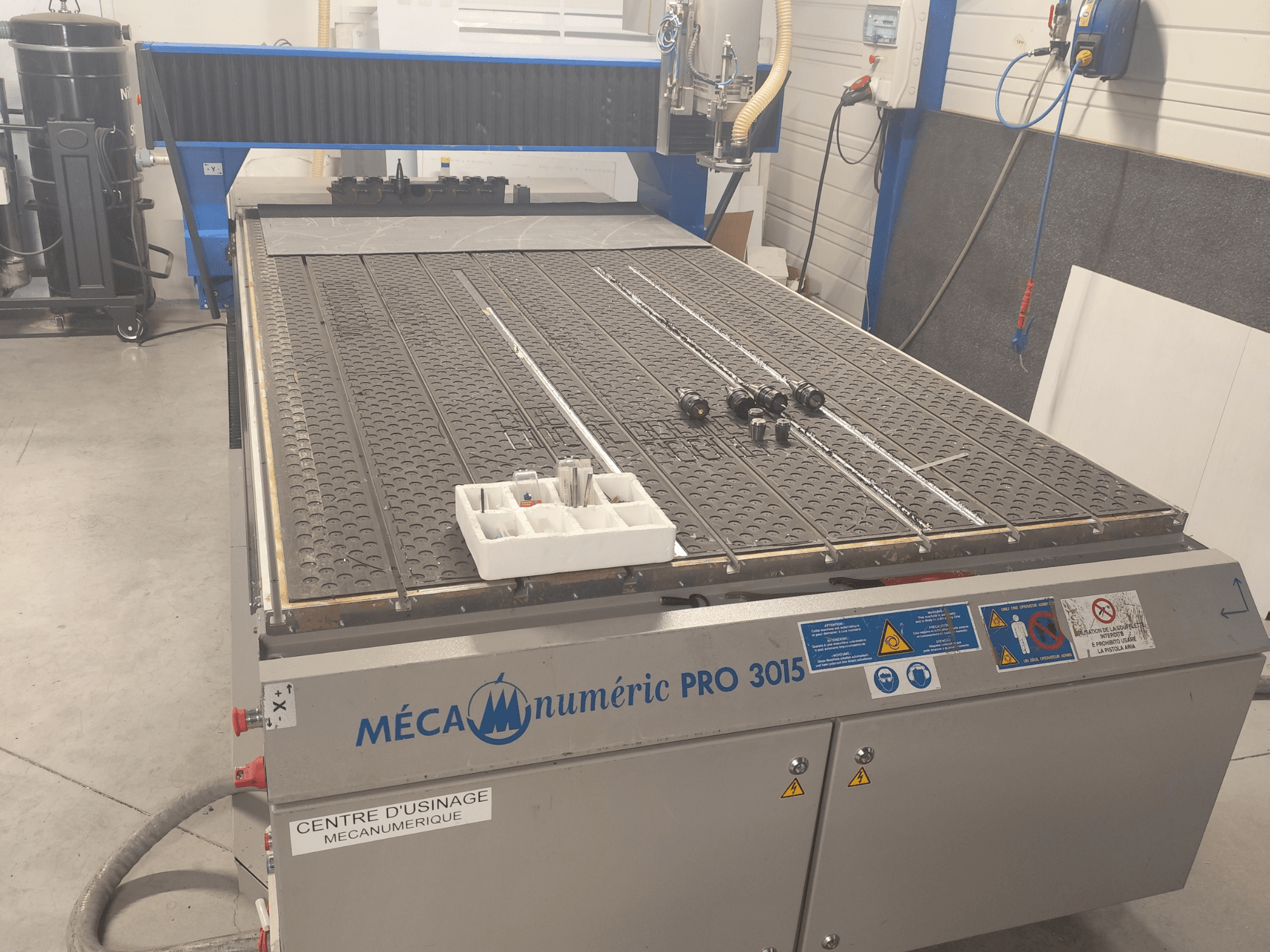 CNC-frees MECANUMERIC Pro 3015 vaade eest, millel on näha üksikasjalikult kujutatud tööpind, juhtpaneel ja laual olevad lisaseadmed.