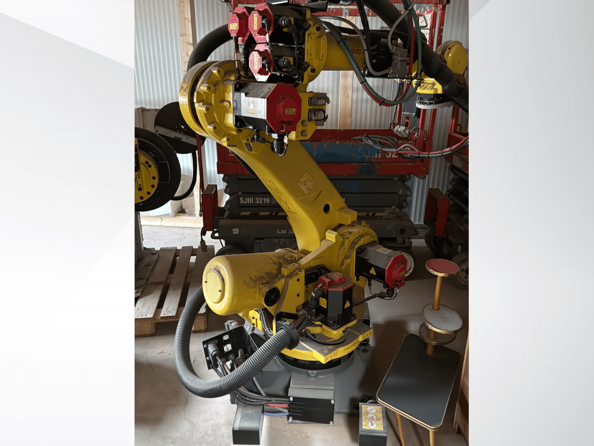 Kollane tööstuslik robotkäsi punaste kontrolleritega, esiplaanil; mitmete liigeste ja voolikutega, seatud tööplatsile.