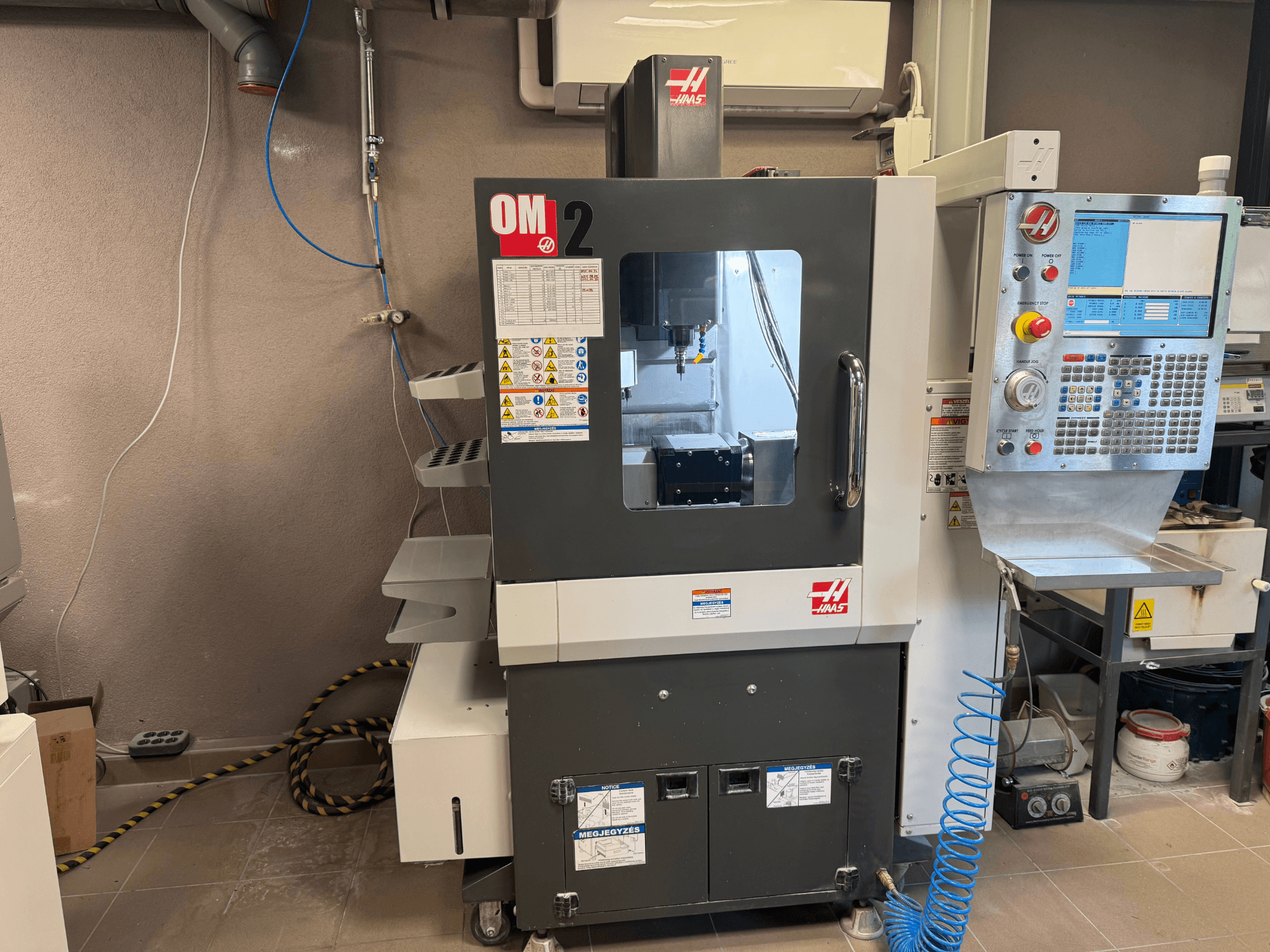 Haas OM-2 CNC-pink, esiplaan, juhtpaneel, spindel ja ohutusmärgised, seadistatud töökojakeskkonnas.