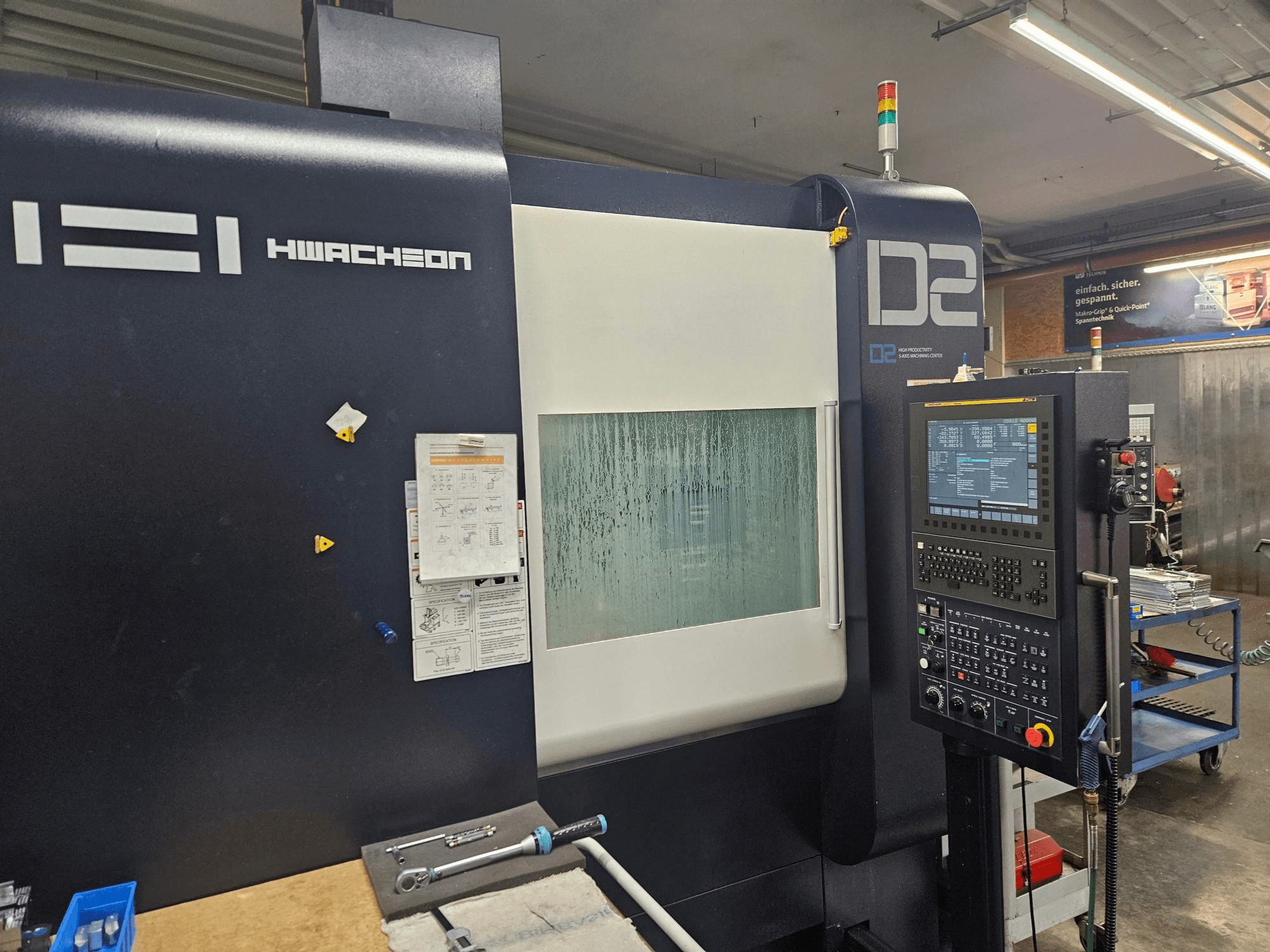 HWACHEON D2-5AX 12k vertikaalne töötlemiskeskus, vaade eest, millel on näha juhtpaneel ja udune vaatamisaken.