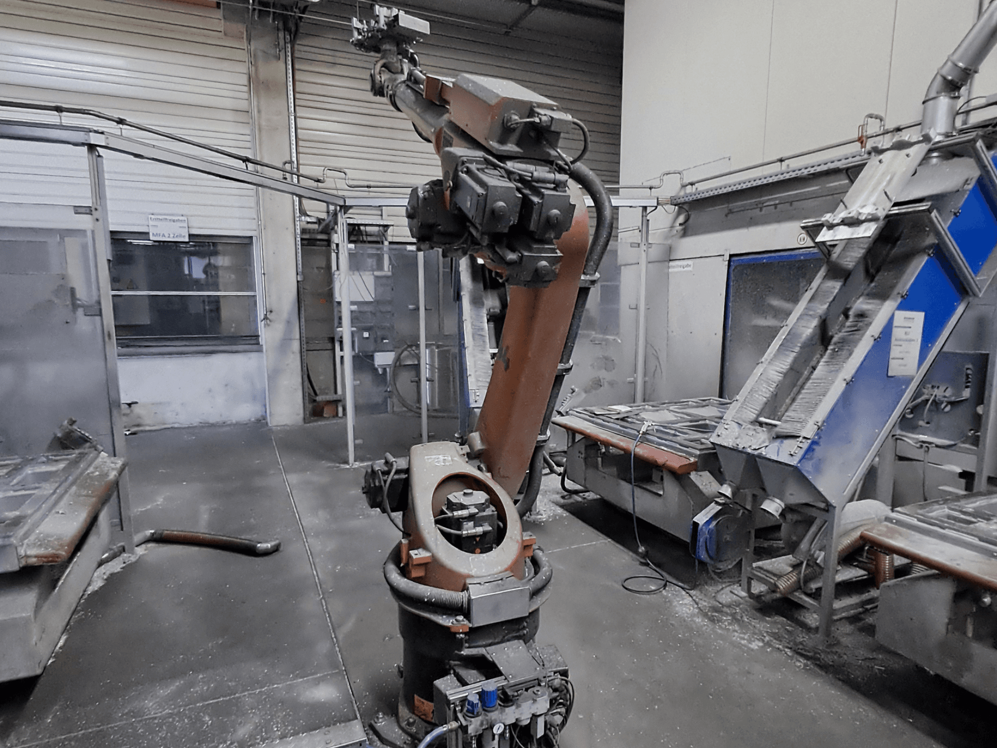 KUKA KR 30L16-2 robotkäsi töökoda-keskkonnas, vaade eest, taustal on näha tolmu ja tööpinkide.