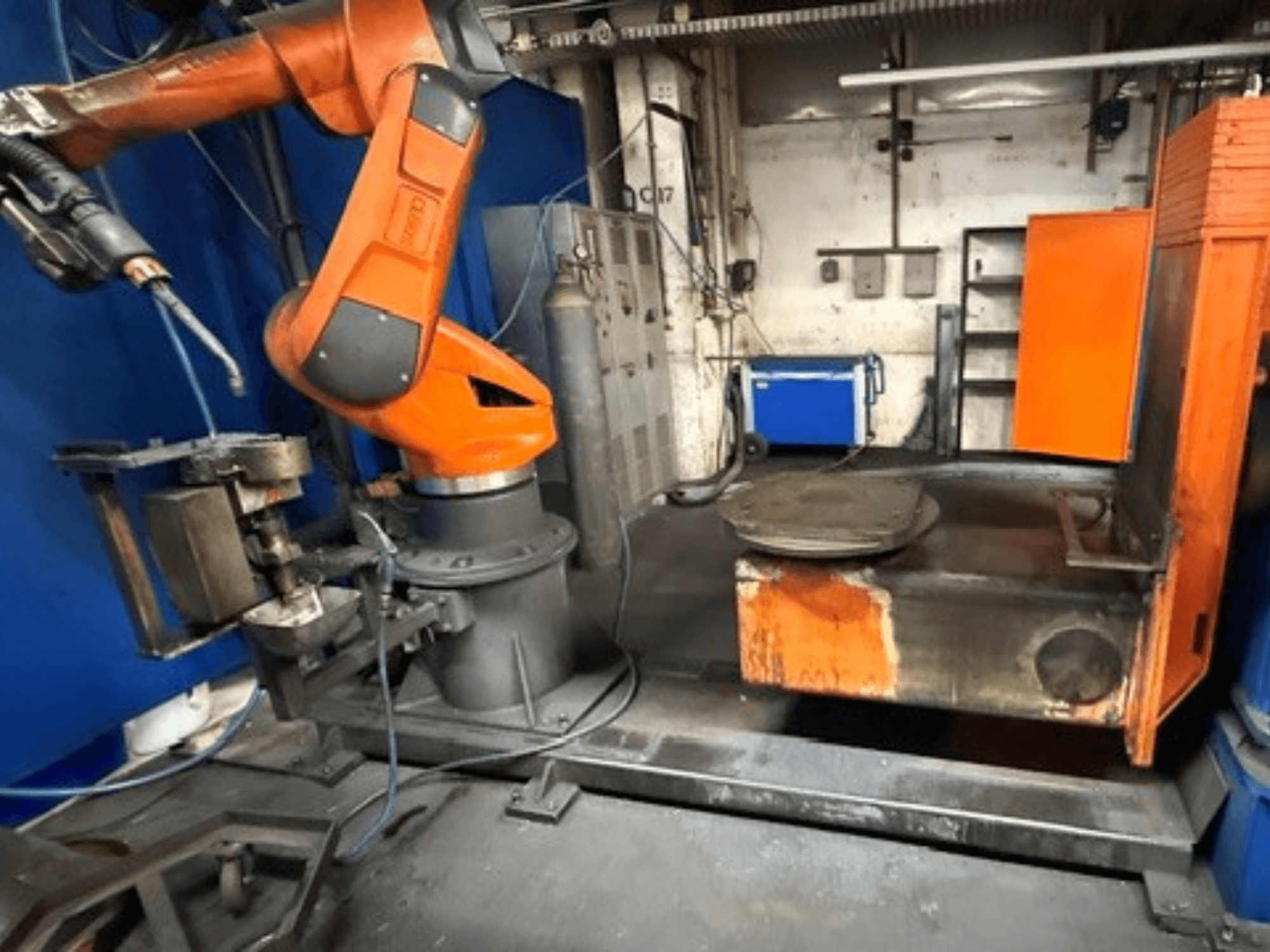 CLOOS C50 keevitusrobot vaadatuna eest, millel on oranž robotkäsi ja metallist töölaud.