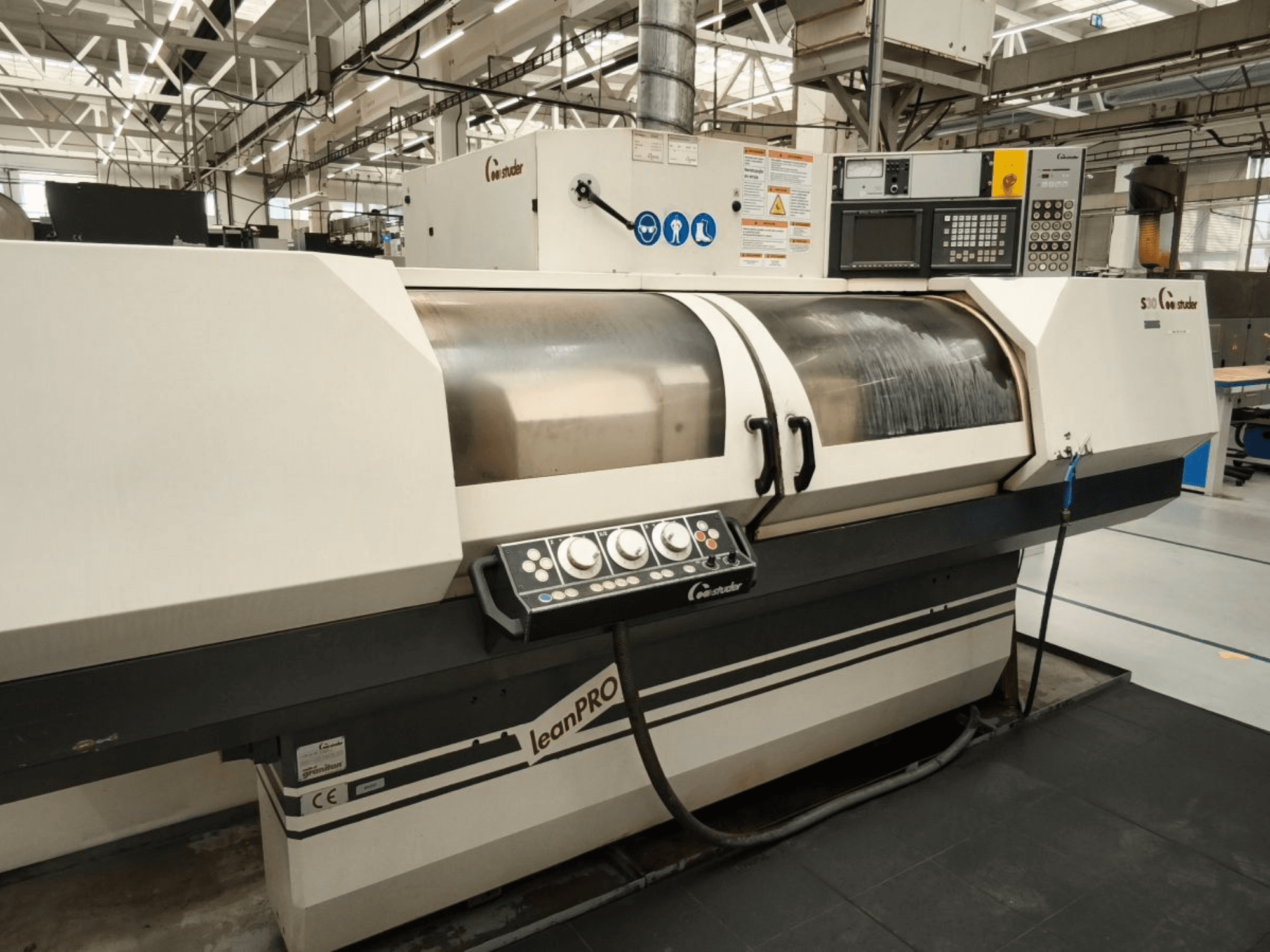 STUDER S30 LEAN PRO silindriline lihvimismasin, külgvaade, kus näidatakse juhtpaneeli ja lihvimisratta katet tööstuslikus keskkonnas.