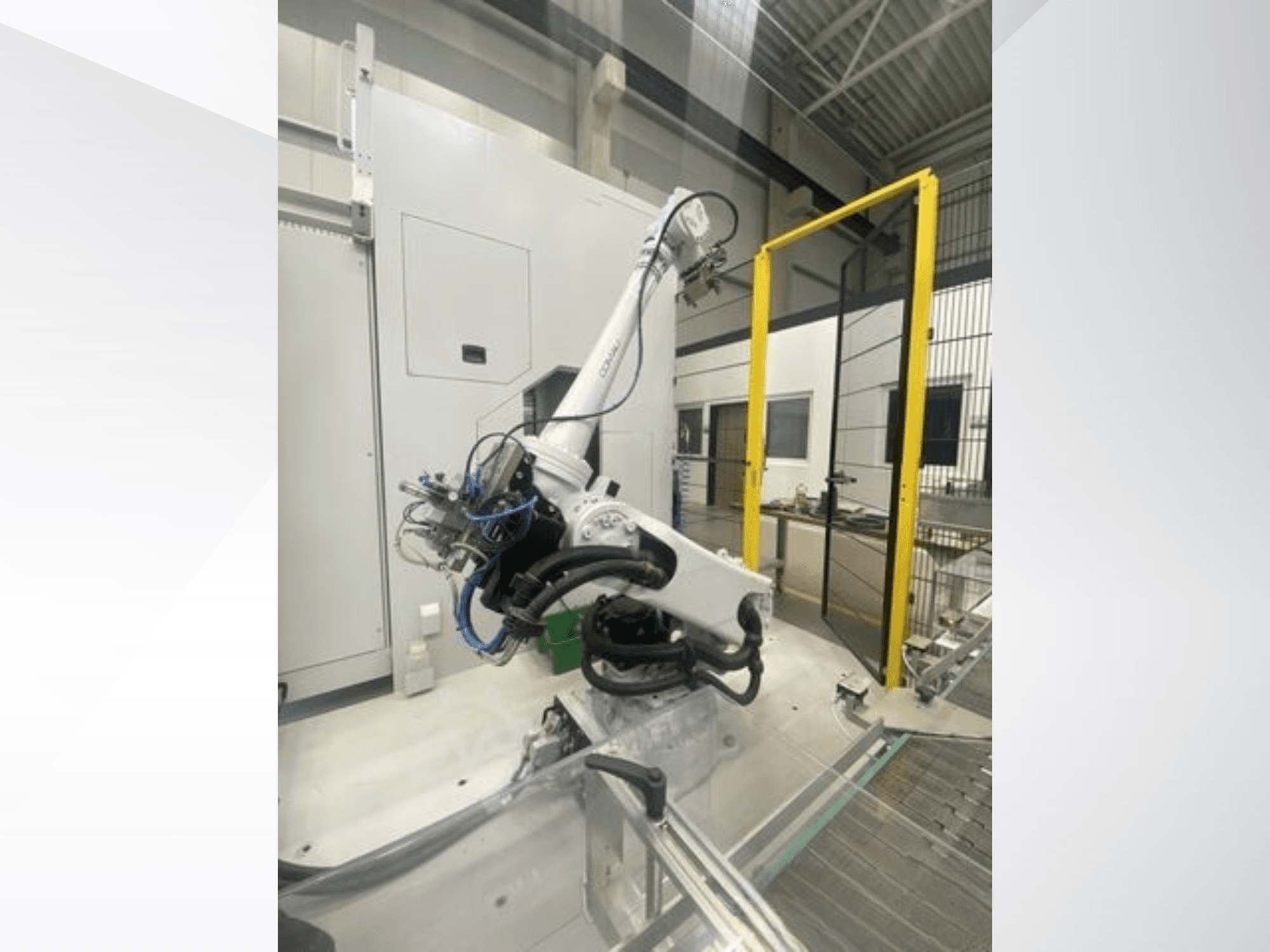 COMAU Smart NJ 40-2.5 robotkäsi külgvaates, millel on kaablid ja kollane turvavärav tehases.
