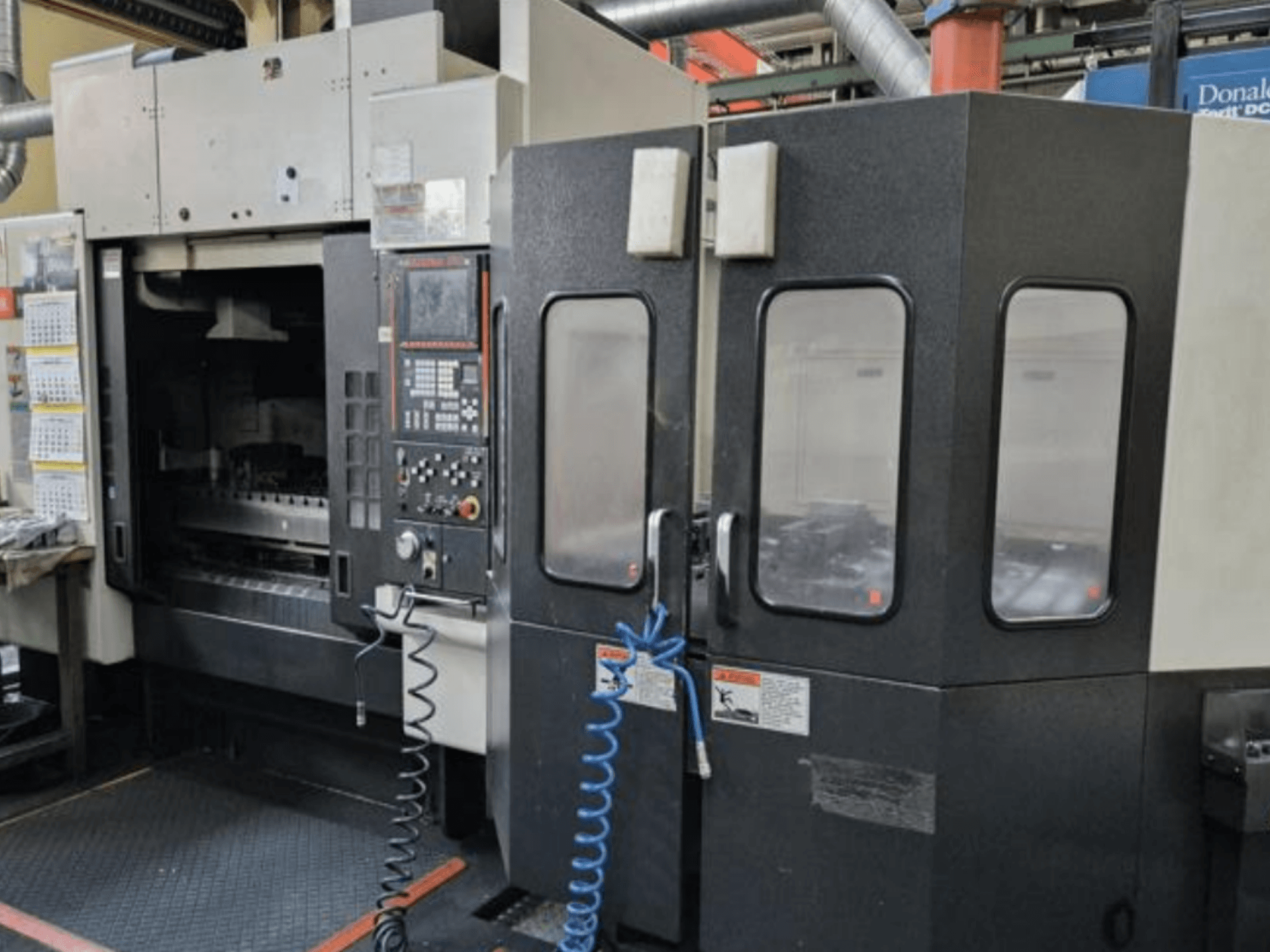 Mazak V515/40N vertikaalne töötlemiskeskus esiplaanil, millel on juhtpaneel ja suletud tööala.