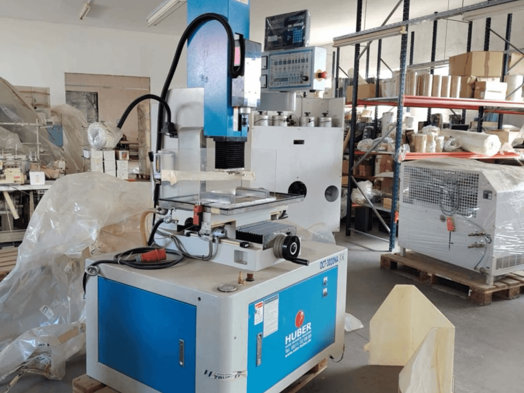 HUBER OCT-3020 NA stantsimispingi sinkpinkimismasin töökojas, esiplaanil sinine ja hall korpus, digitaalsed juhtimisseadmed ja tööpiirkond.