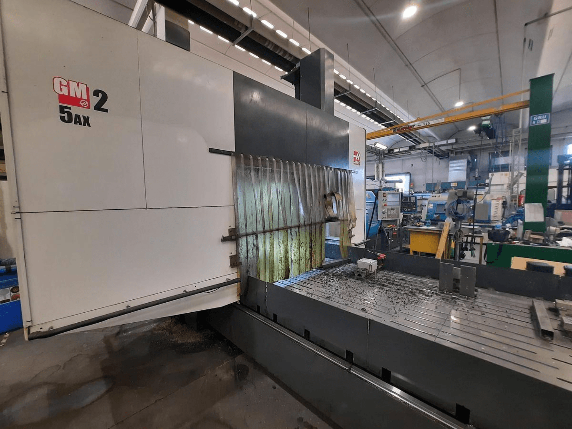 GM 2 5AX CNC-tööpink töökojas, külgvaade, kus on näha tööpiirkond ja metallilaastud töölaua pinnal.
