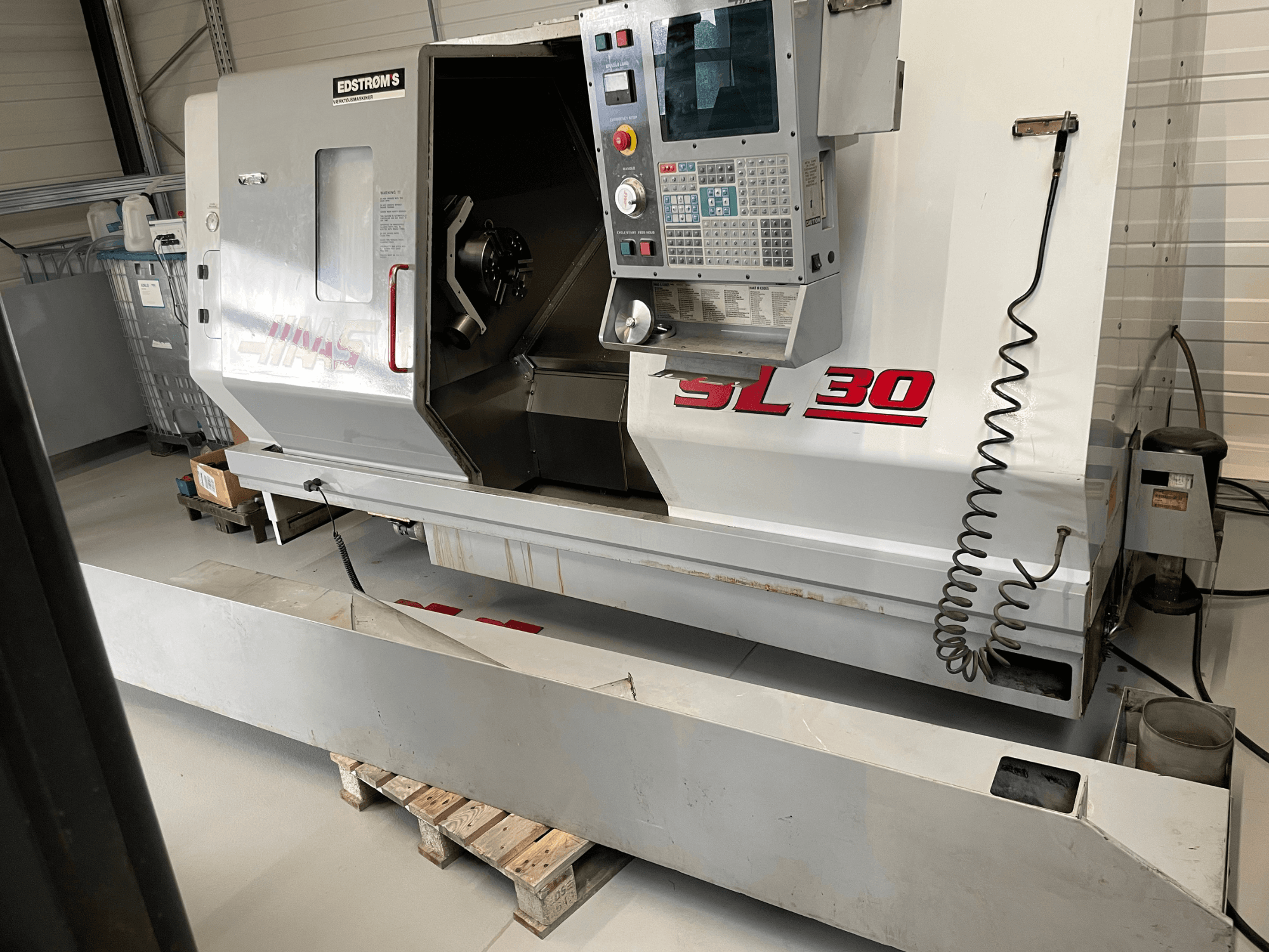 Haas SL 30 CNC-teenindusega treipink töökojas, külgvaade, kus on juhtpaneel ja avatud spindel töötlemisülesannete jaoks.