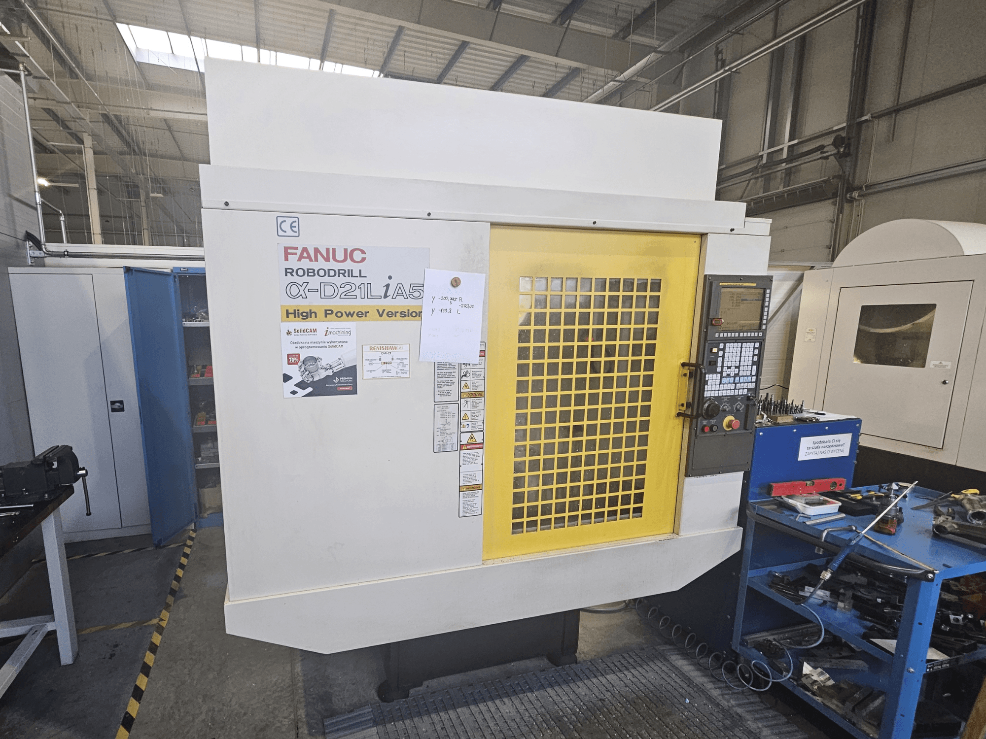 FANUC Robodrill α-D21LiA5 esivaade kollase turvaukse, juhtpaneeli ja tööruumi tööriistade lähedal.