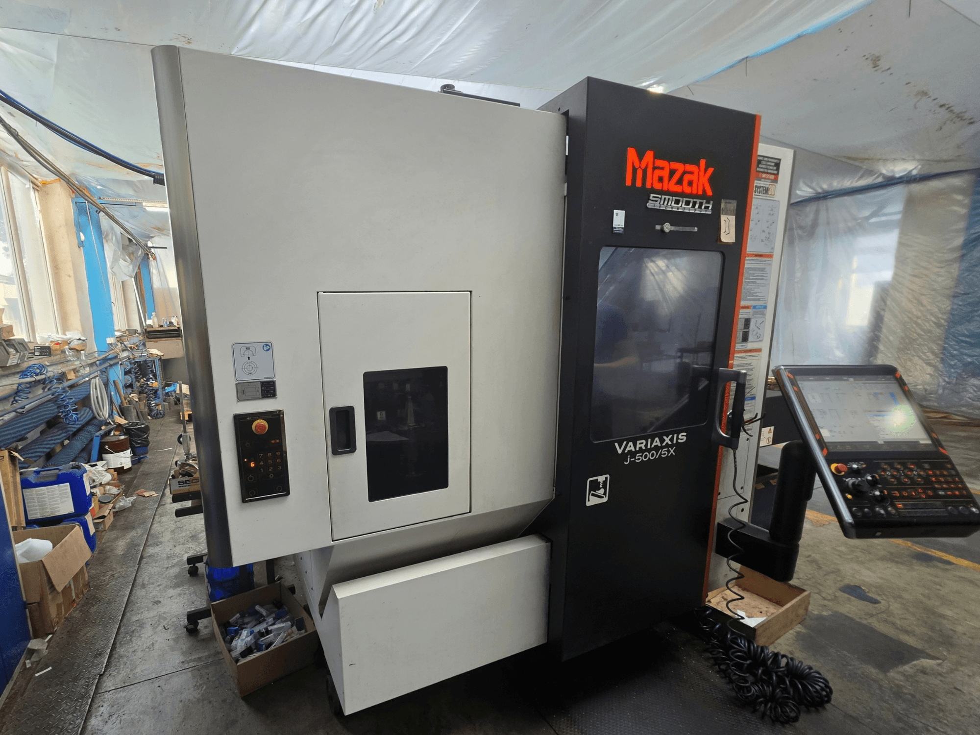 Mazak VARIAXIS J-500/5X vertikaalne töötlemiskeskus, külgvaade, millel on näha juhtimispaneelid ja ekraan, paigaldatud töökoda keskkonnas.
