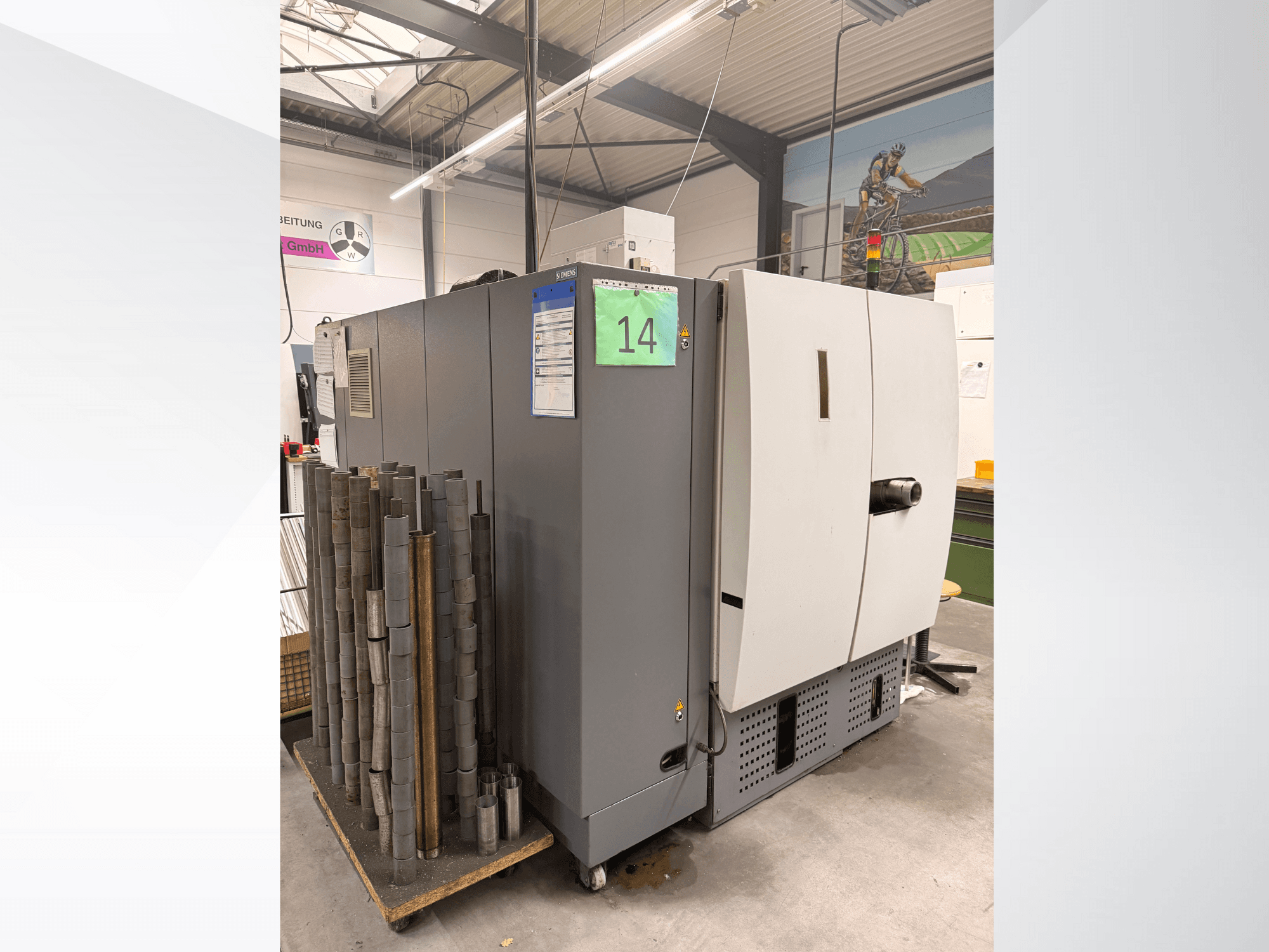 Siemens'i hall tööstusmasin, külgvaade, kõrval silindriliste metallitükkide laos ja nähtavad seadmete sildid.