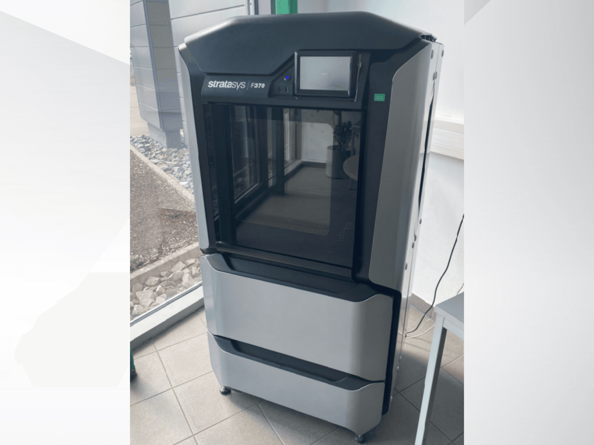 Stratasys F370 plastikust 3D-printer, esiplaanil, mis näitab elegantset musta ja halli disaini koos puuteekraaniga.
