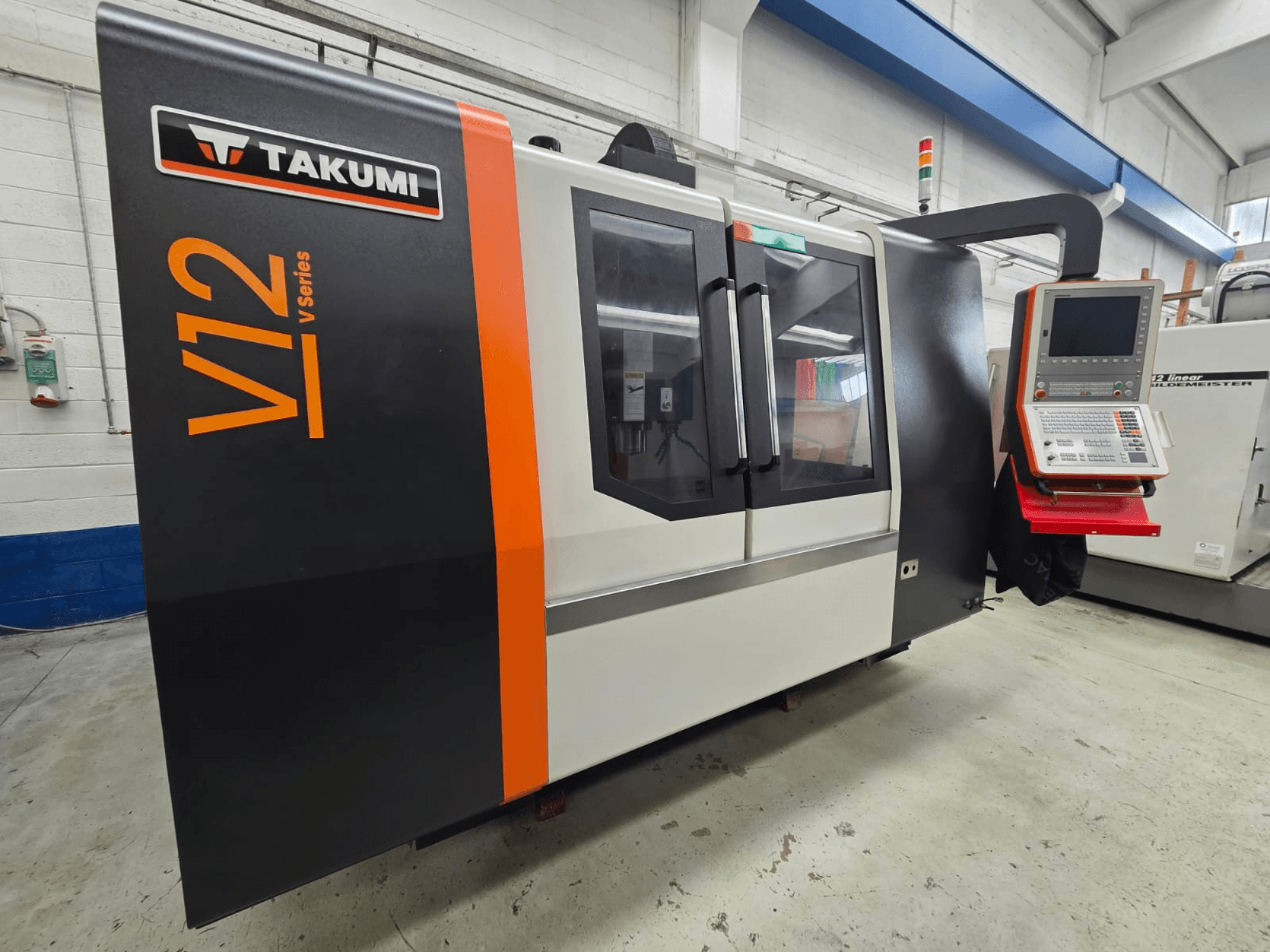 Takumi V12 V-seeria CNC-freespingi esivaade, millel on juhtpaneel ja suured klaasaknad.