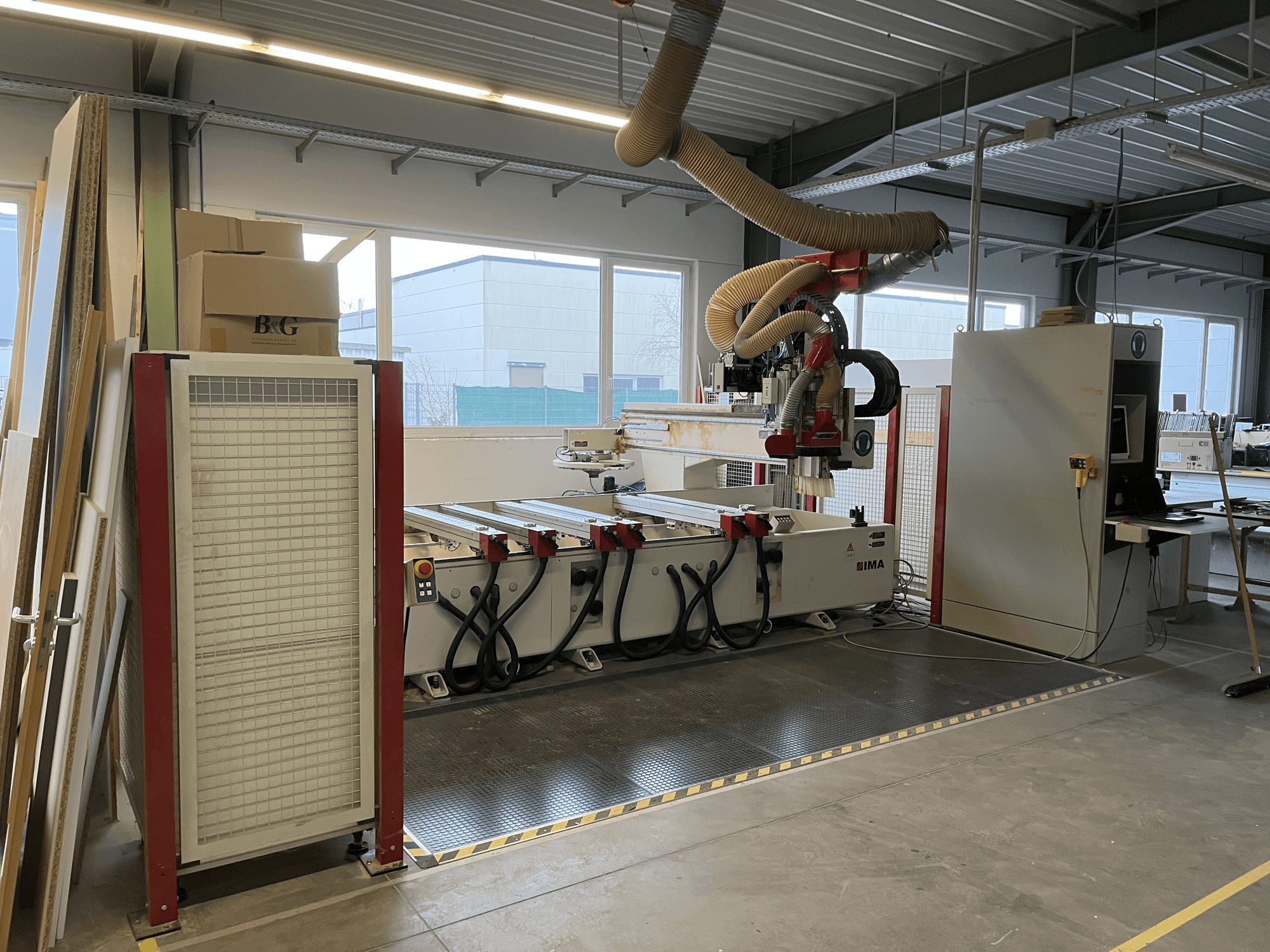 CNC-puidutöötluskeskus IMA BIMA 410 töökojas, külgvaade, kus on näha juhtpaneel ja tolmuimejasüsteem.