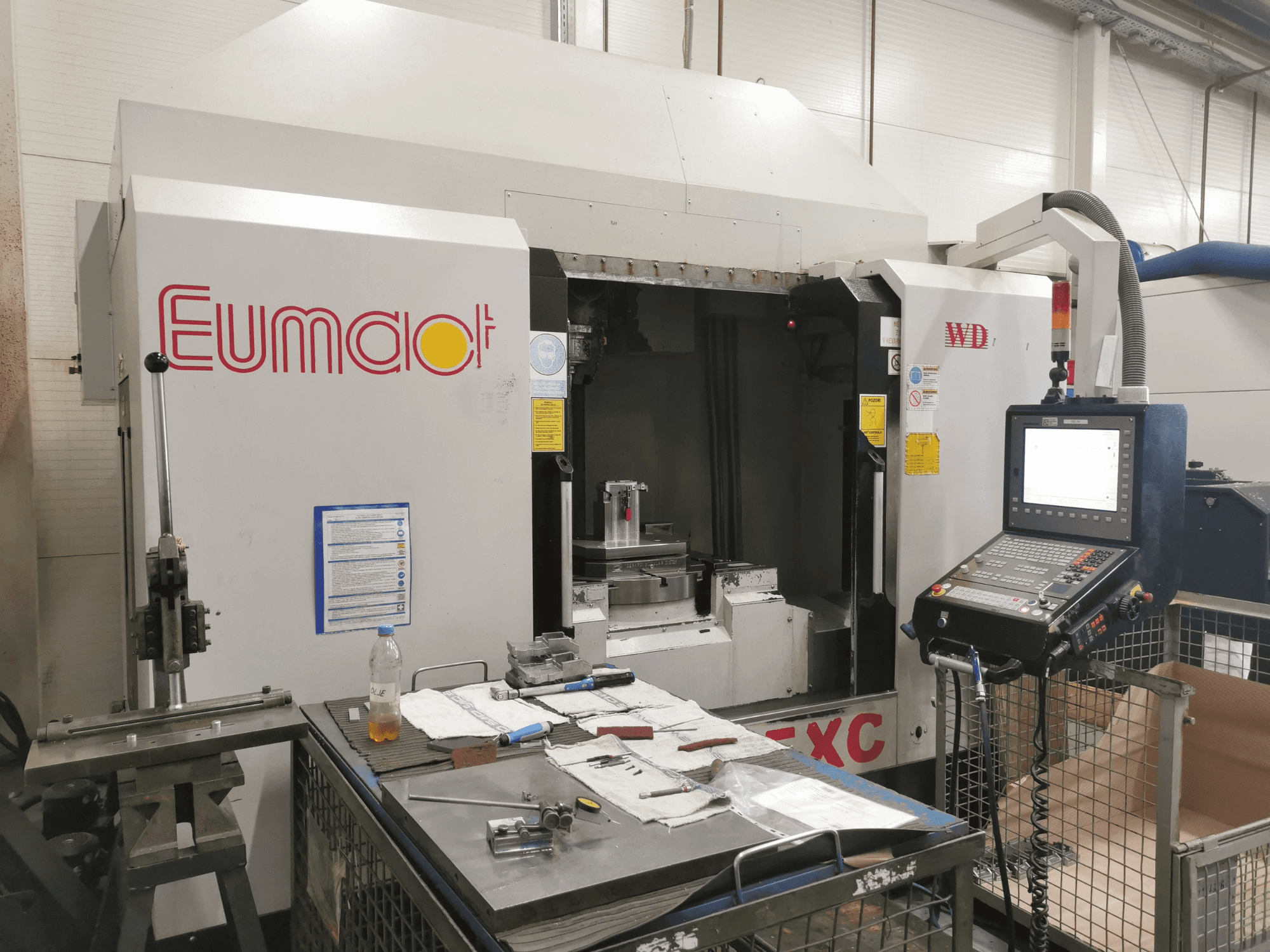 Eumdaot CNC-pingi esivaade koos juhtpaneeli, tööriistade ja tööpinnaga, mis on täis komponente ja materjale.