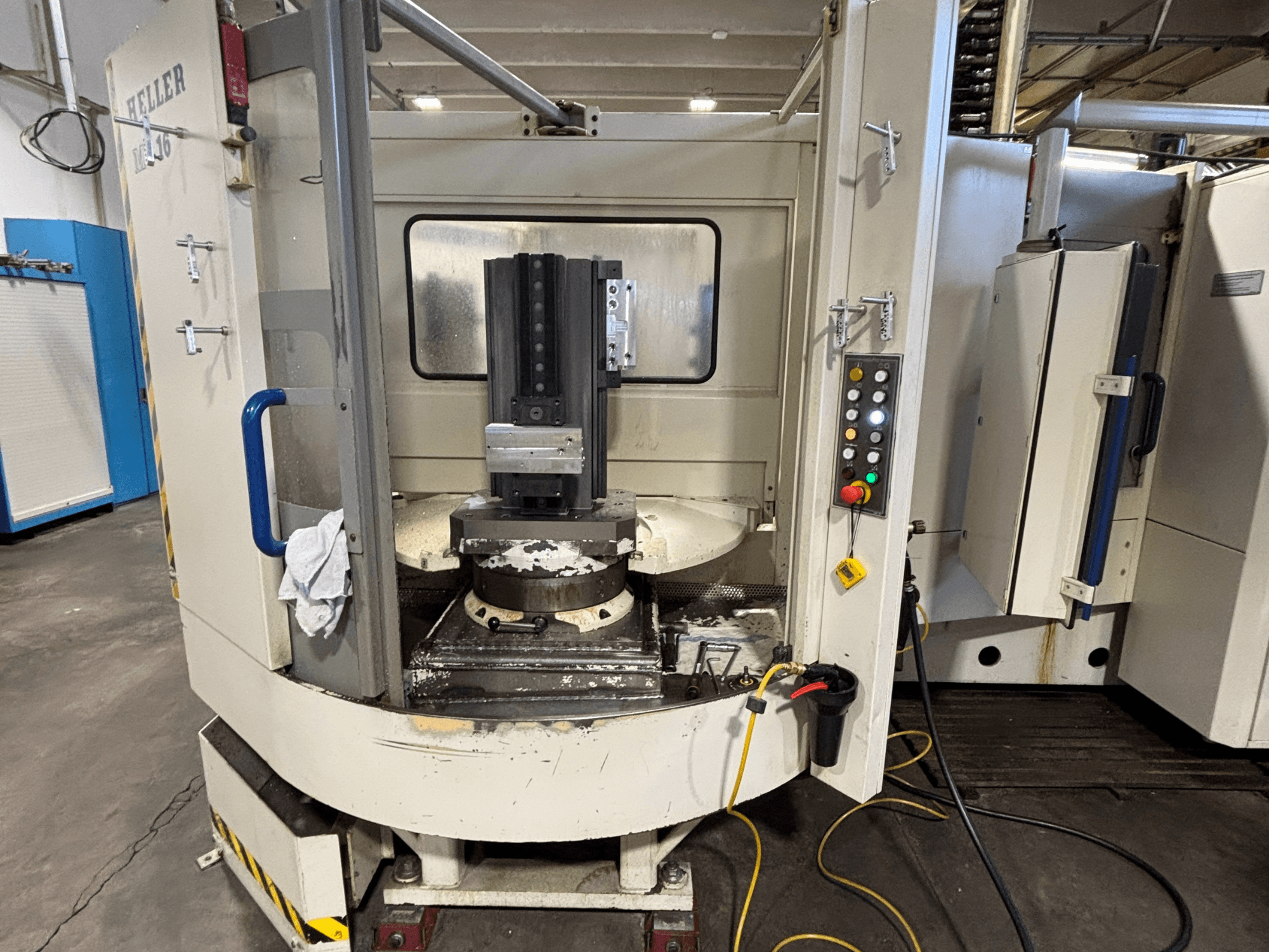 Heller töötluskeskus, mudel vertikaalne, esivaade, kus on näidatud spindel, juhtpaneel ja töölaud koos kinnitatud seadmetega.