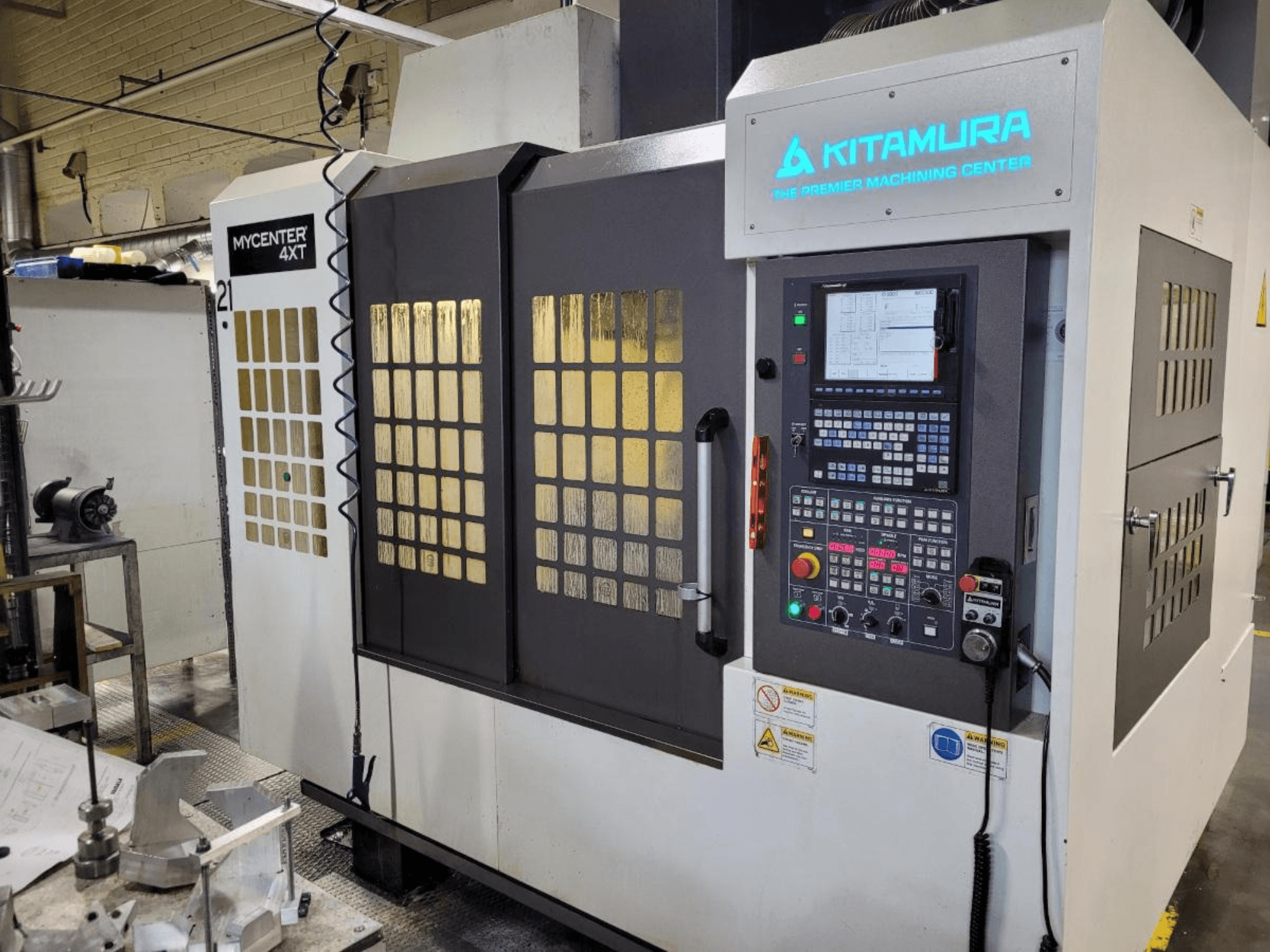 Vertikaalne vaade Kitamura Mycenter-4XT töötlemiskeskusele, millel on juhtpaneel ja valgustatud kaubamärk.