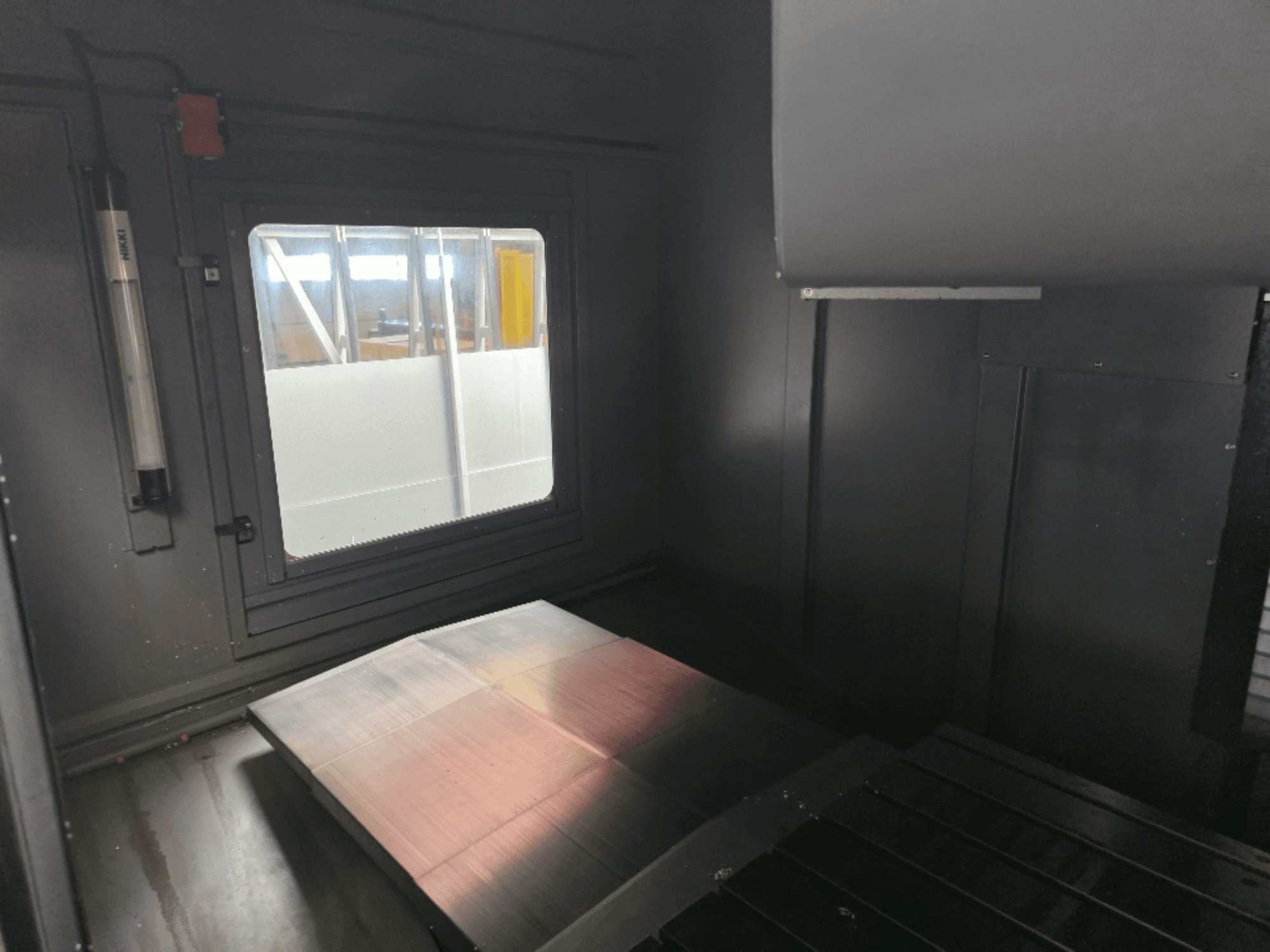 Lihvitud metallplaadi, külgakna ja minimaalse valgustusega masinakarbi sisevaade. Marki ei ole näha.